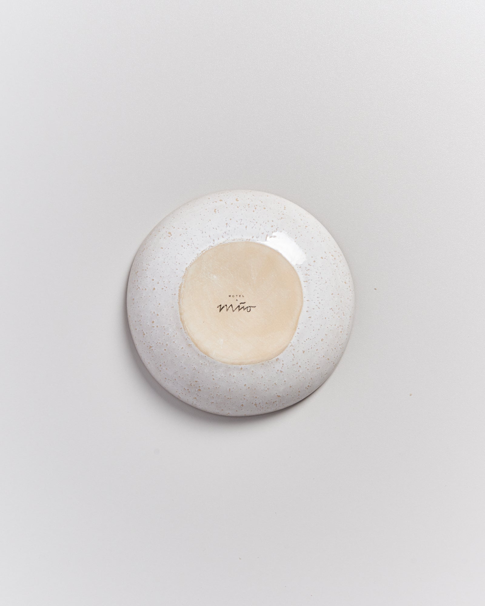Ein runder Keramikteller mit der Aufschrift „Hotel Miro“ auf der Unterseite, auf einem hellen Hintergrund.