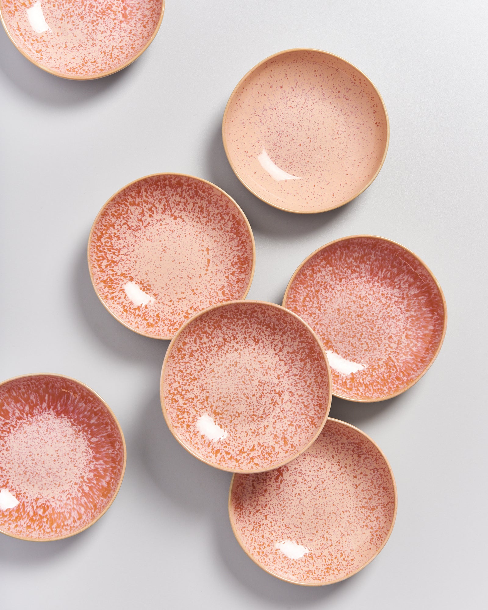 Sieben rosa, gesprenkelte Teller liegen auf einem grauen Hintergrund.