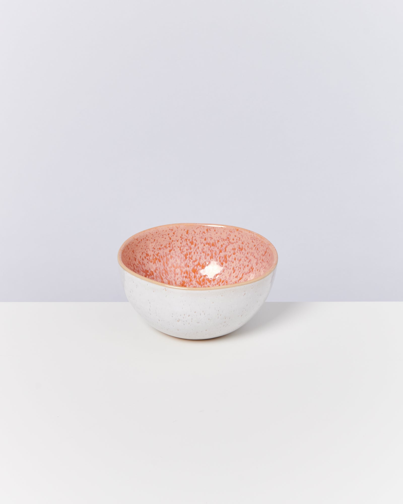 Keramikschüssel mit rosa Sprenkeln im Inneren und weißem Äußeren auf weißem Hintergrund.