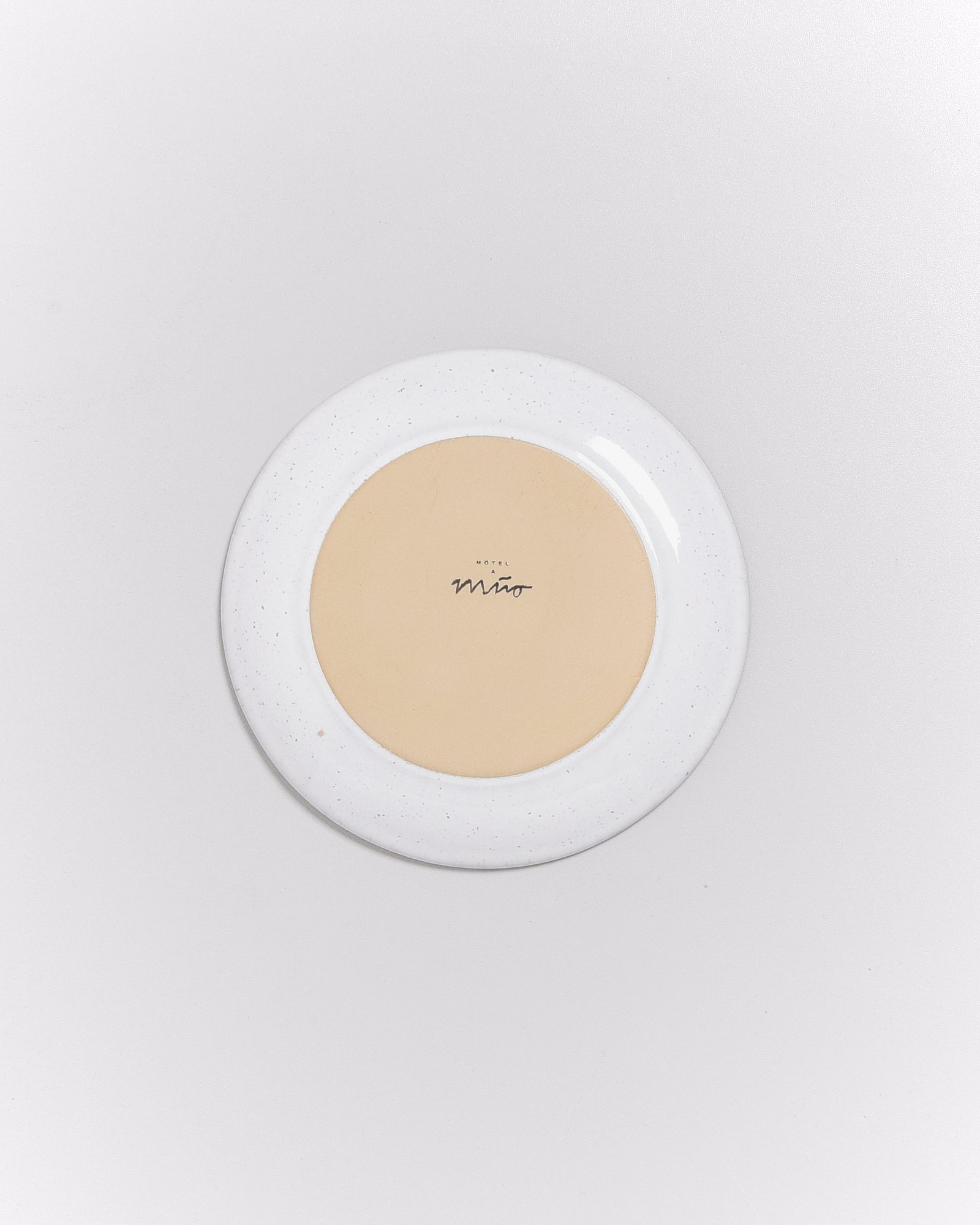 Ein runder Teller mit beigem Zentrum und weißem Rand, auf dem "Hotel Miro" steht.