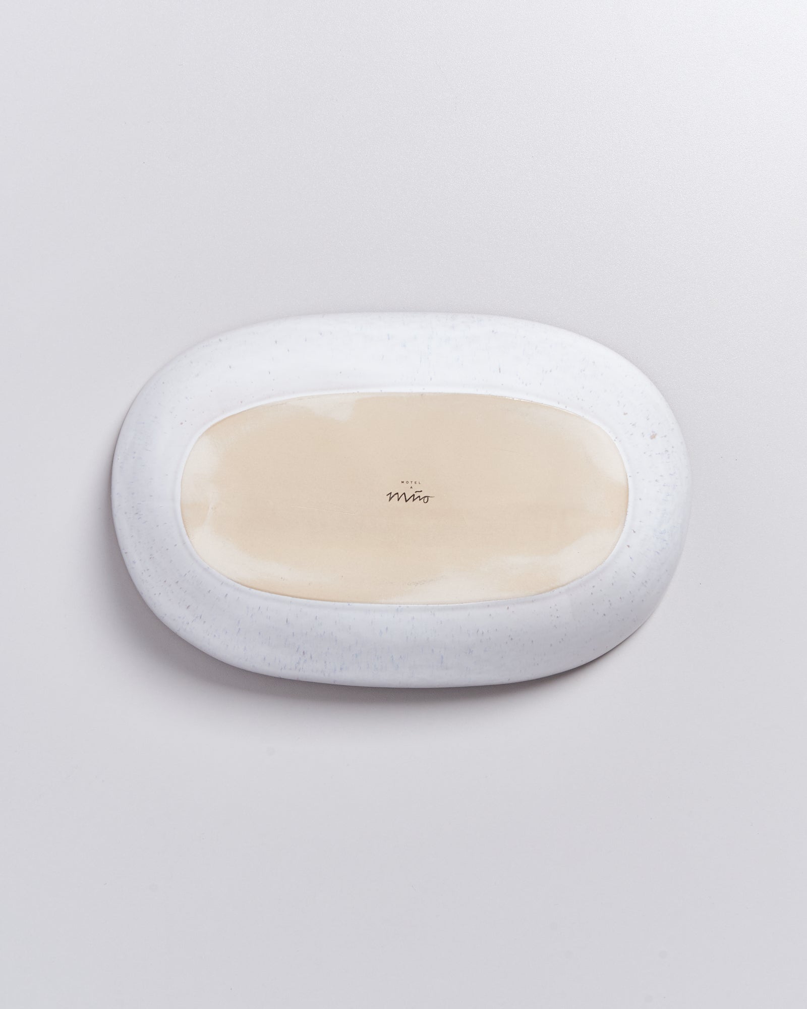 Ovaler Teller mit weißem Rand und beiger Mitte auf hellgrauem Hintergrund.