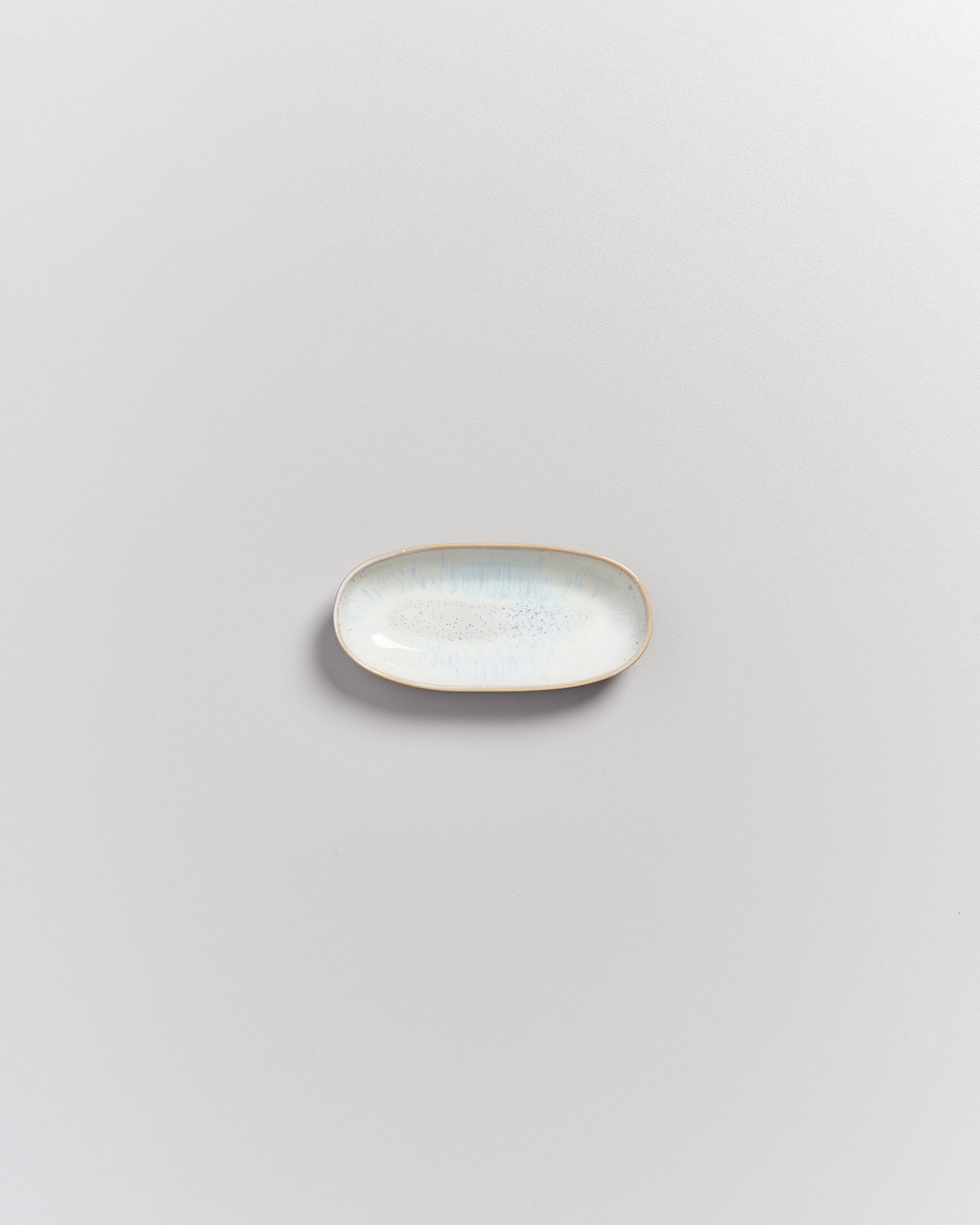 Kleiner ovaler Teller mit hellem, gesprenkeltem Muster auf einer grauen Oberfläche.