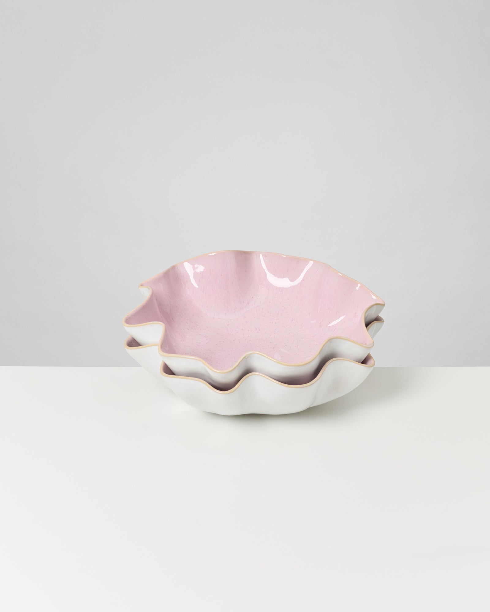Zwei ineinander gestapelte, wellenförmige Schalen mit rosa Innenseite auf einem weißen Tisch.
