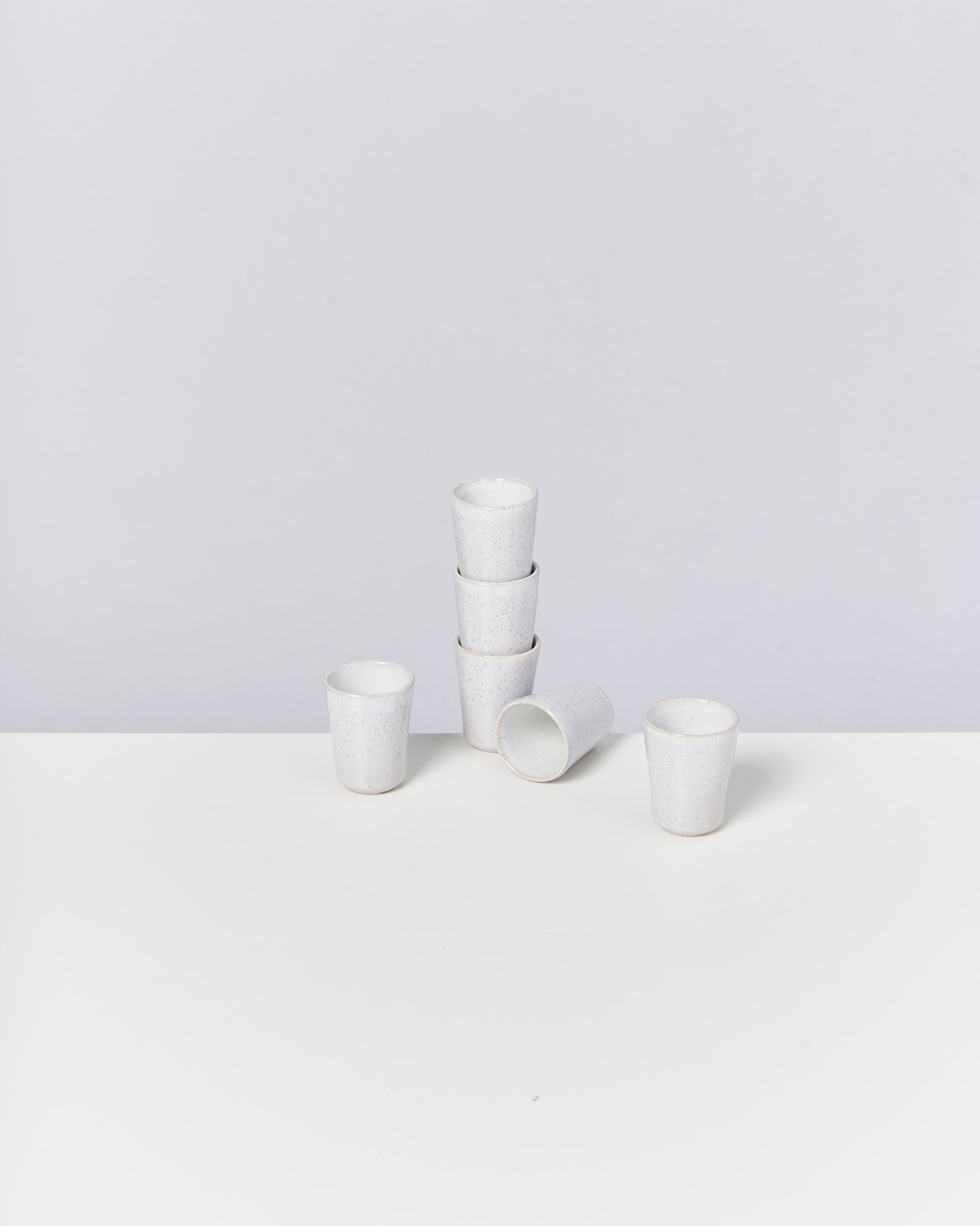 Sechs weiße Becher in verschiedenen Anordnungen auf einem weißen Untergrund vor grauem Hintergrund.