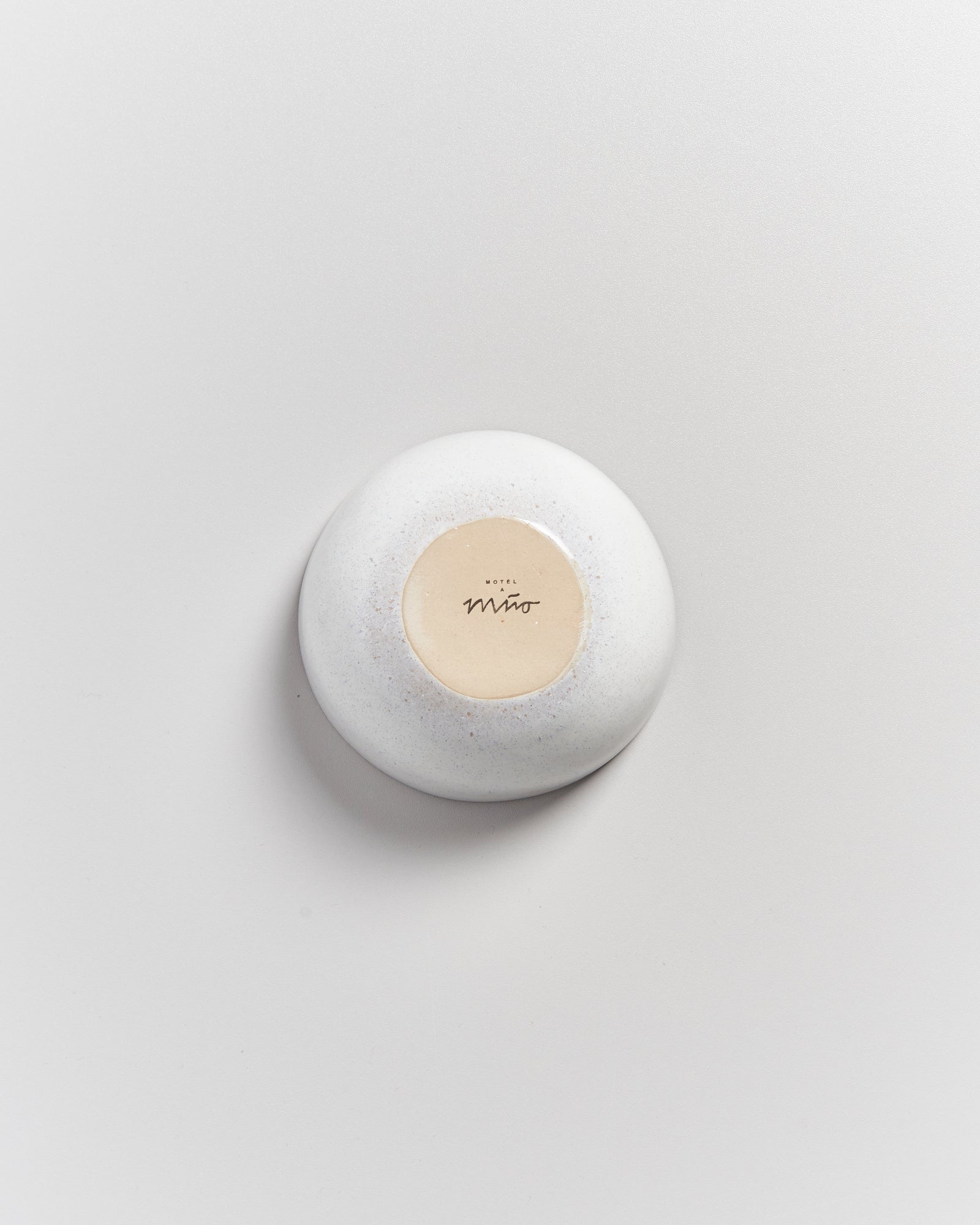 Ein weißer, runder Stein mit einer beige Fläche auf der Oberseite, auf der "Hotel Miro" steht, liegt auf einem weißen Untergrund.