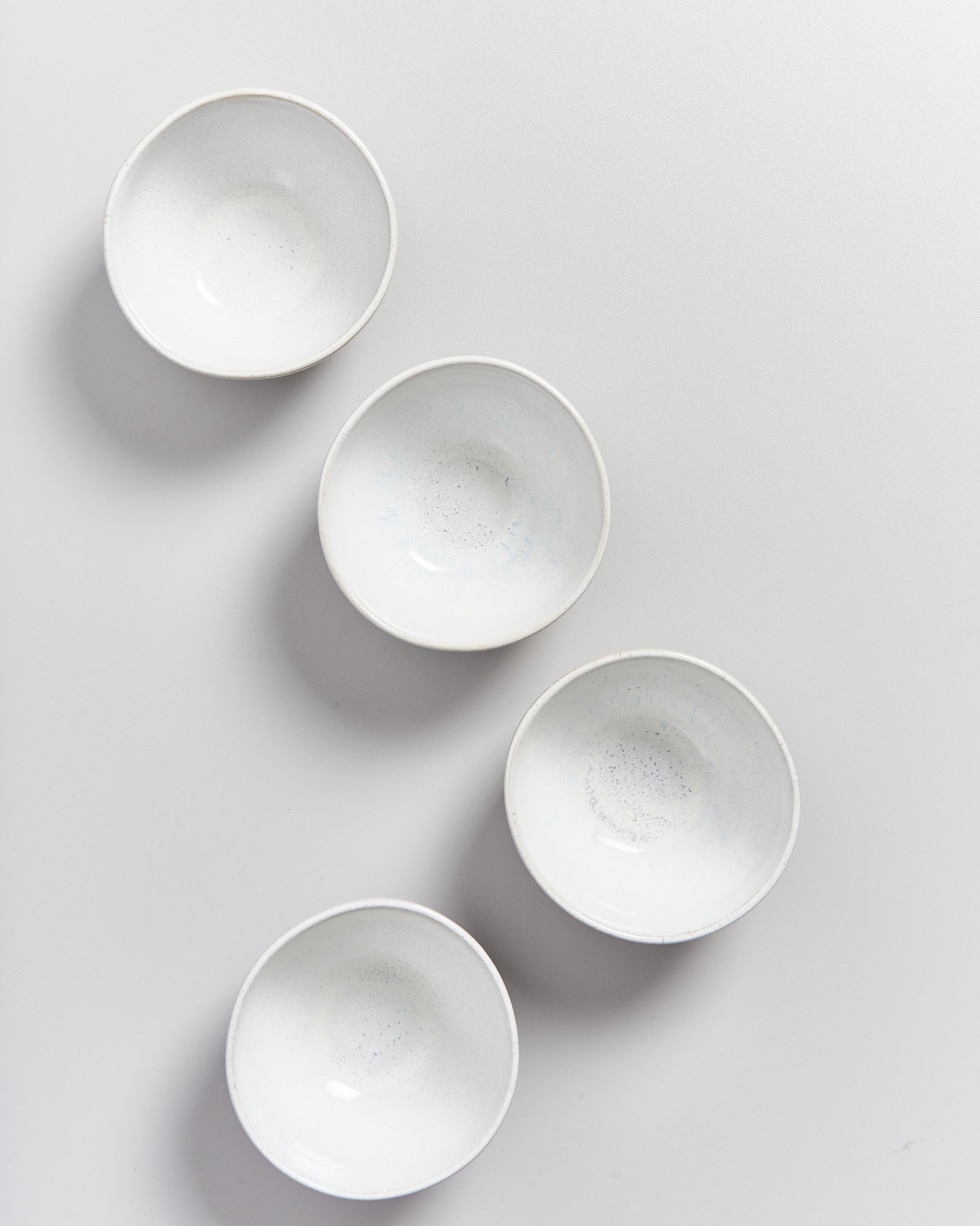 Vier weiße, runde Schalen auf einem hellgrauen Hintergrund in diagonaler Anordnung.