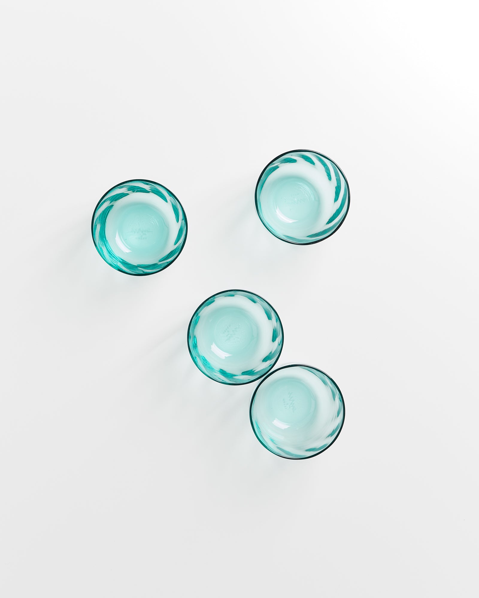 Vier türkisgrüne Glasschalen auf weißem Hintergrund, symmetrisch angeordnet.