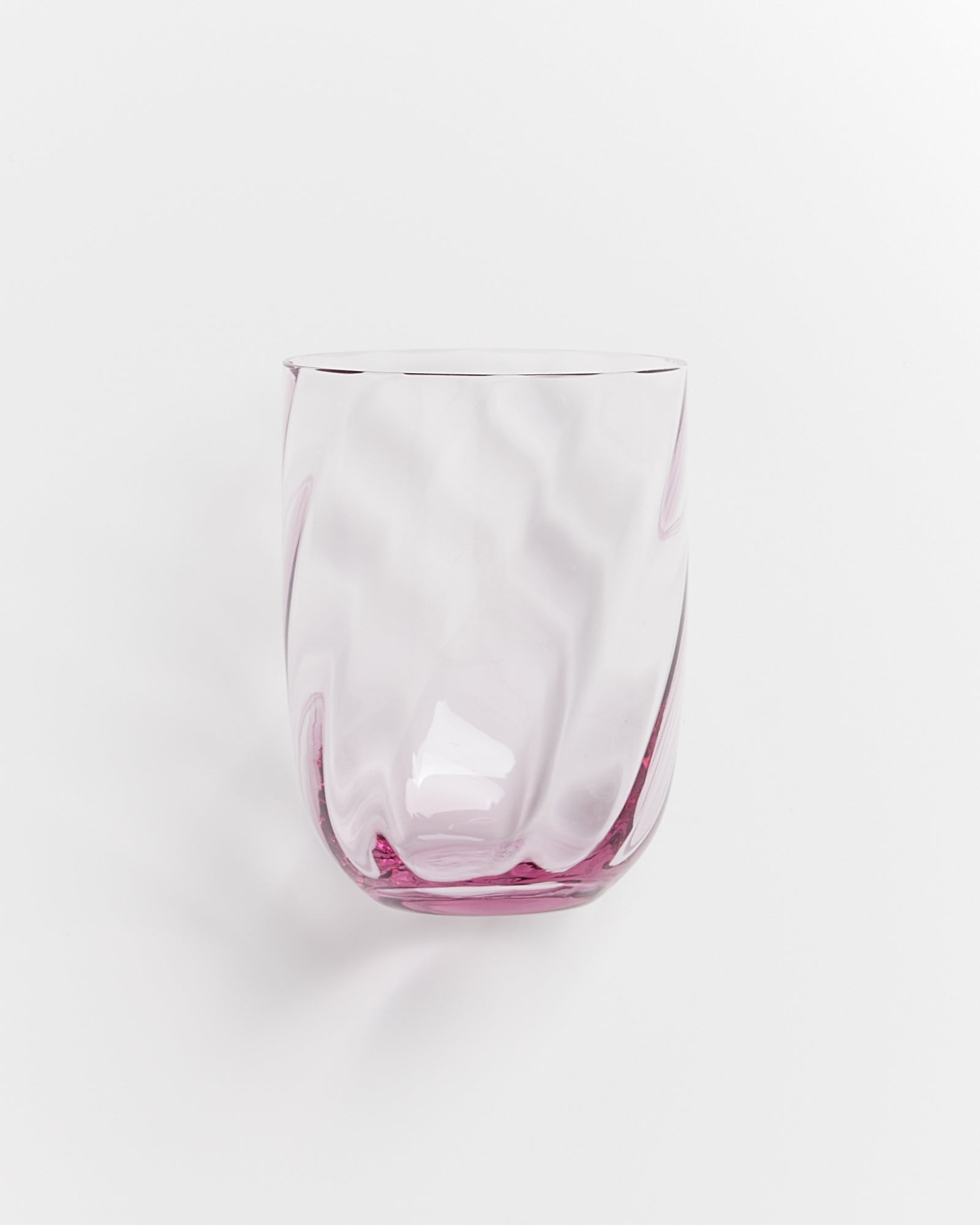 Ein transparentes, leicht rosa Glas mit gewellter Oberfläche vor weißem Hintergrund.