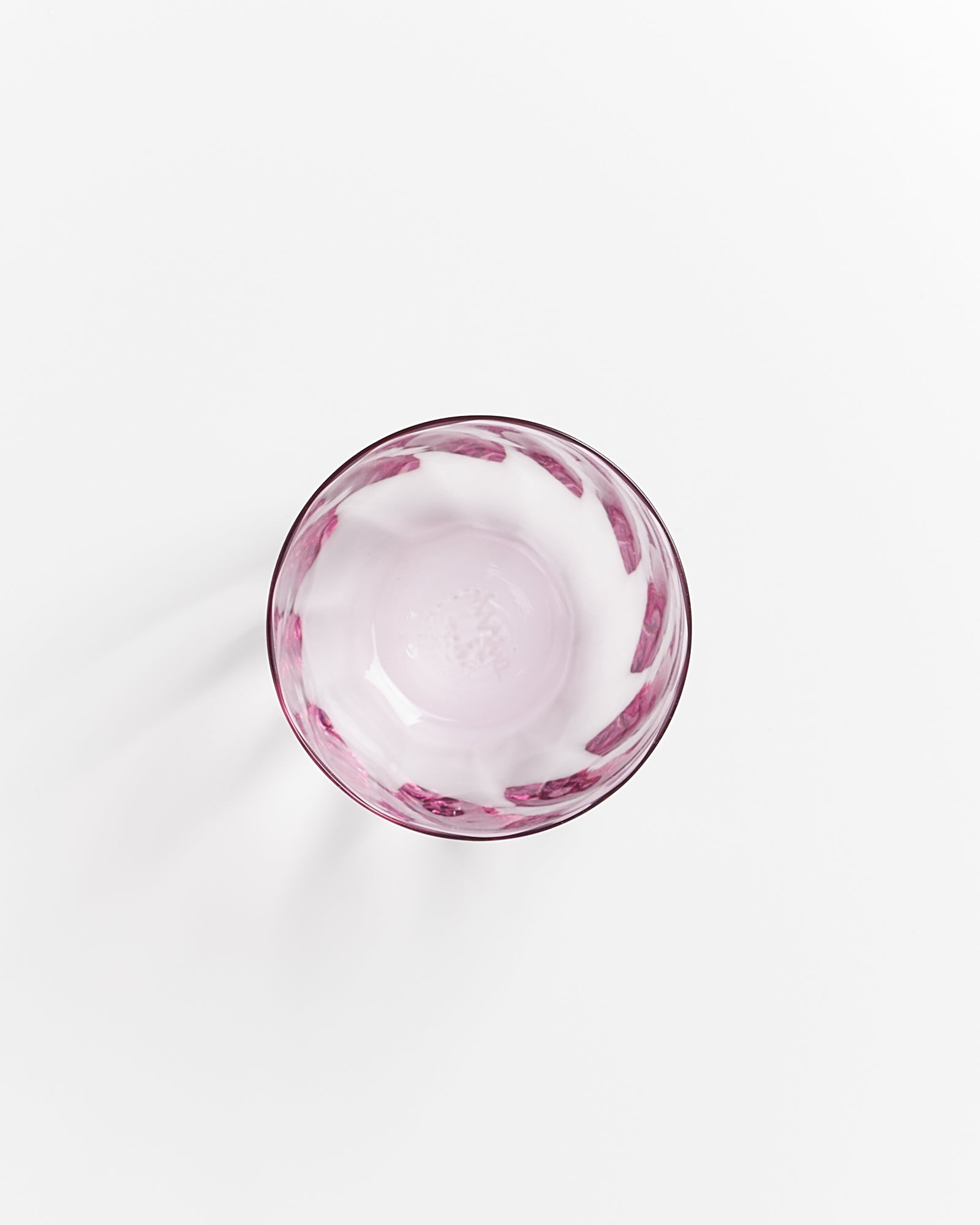 Ansicht von oben auf ein halbvolles, rosafarbenes Glas mit einem Muster auf hellem Hintergrund.