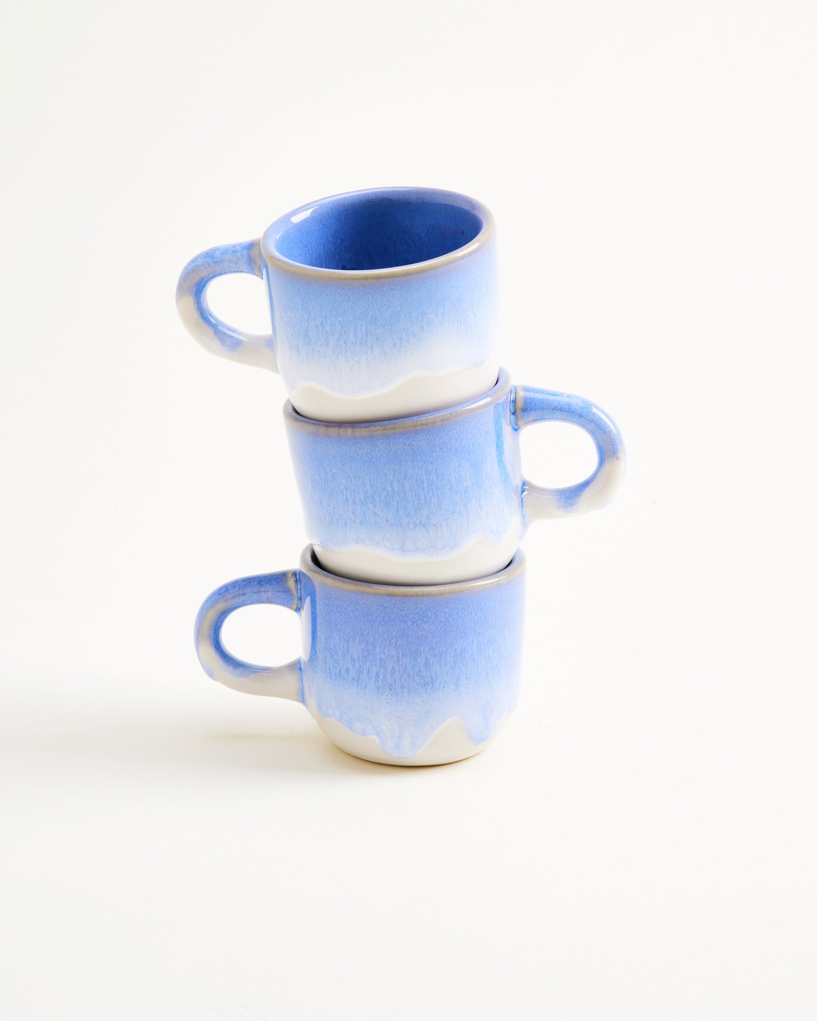 Drei gestapelte blaue Tassen mit weißem Muster auf weißem Hintergrund.