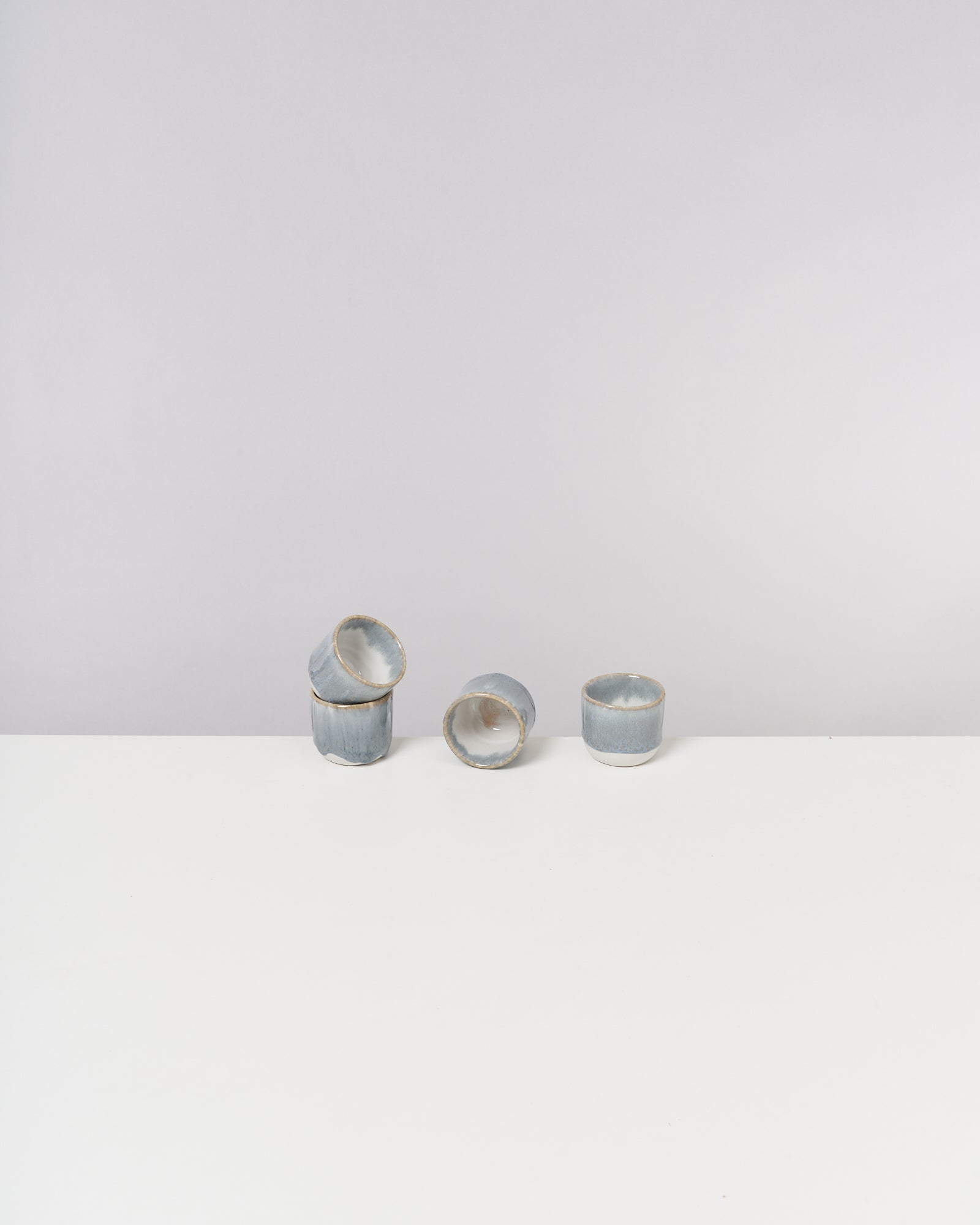Drei blaue Keramiktassen stehen auf einem weißen Tisch, eine davon liegt auf der Seite.