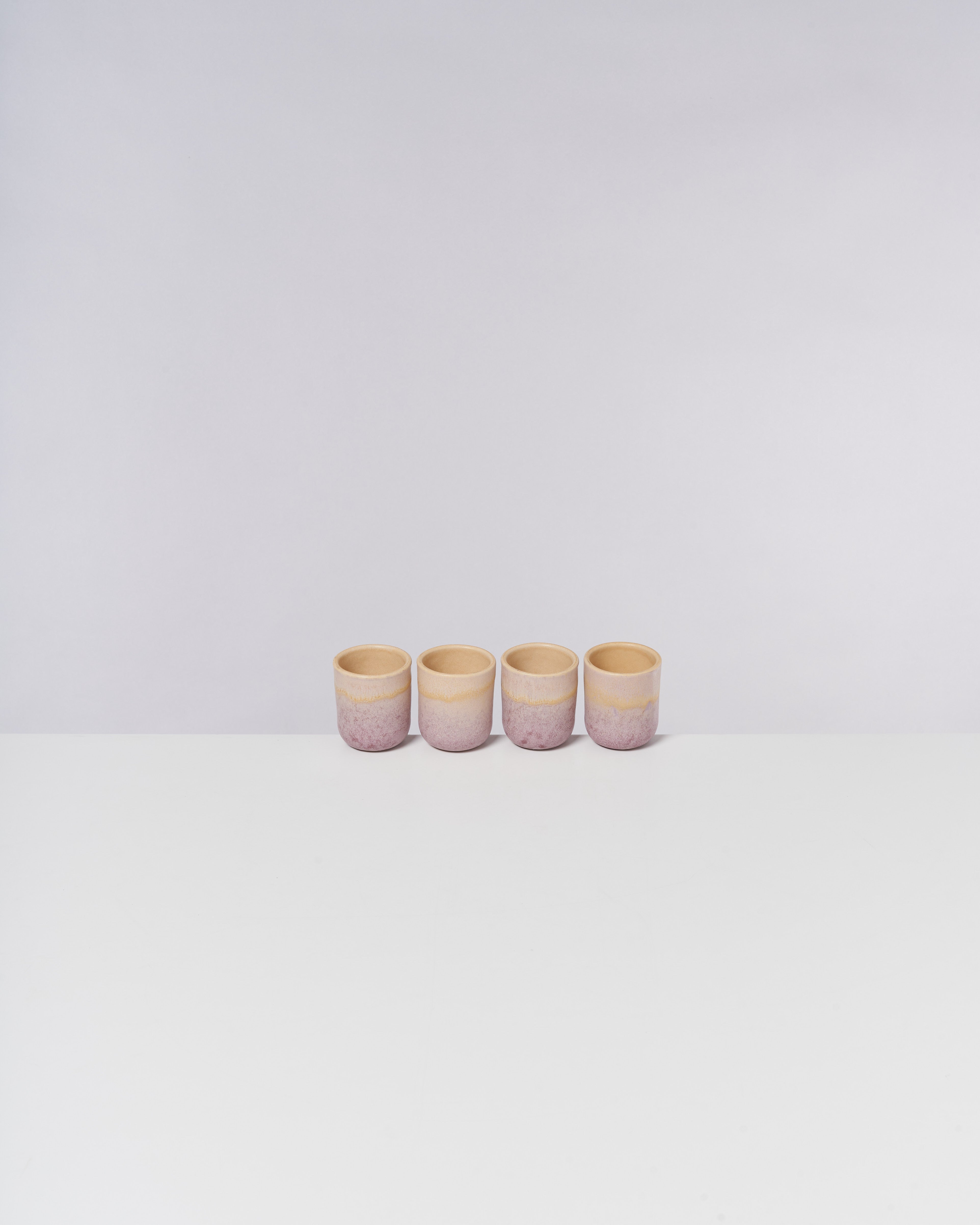 Vier kleine, becherartige Gefäße mit einem blassrosa und cremefarbenen Verlauf, aufgereiht auf einem weißen Tisch.