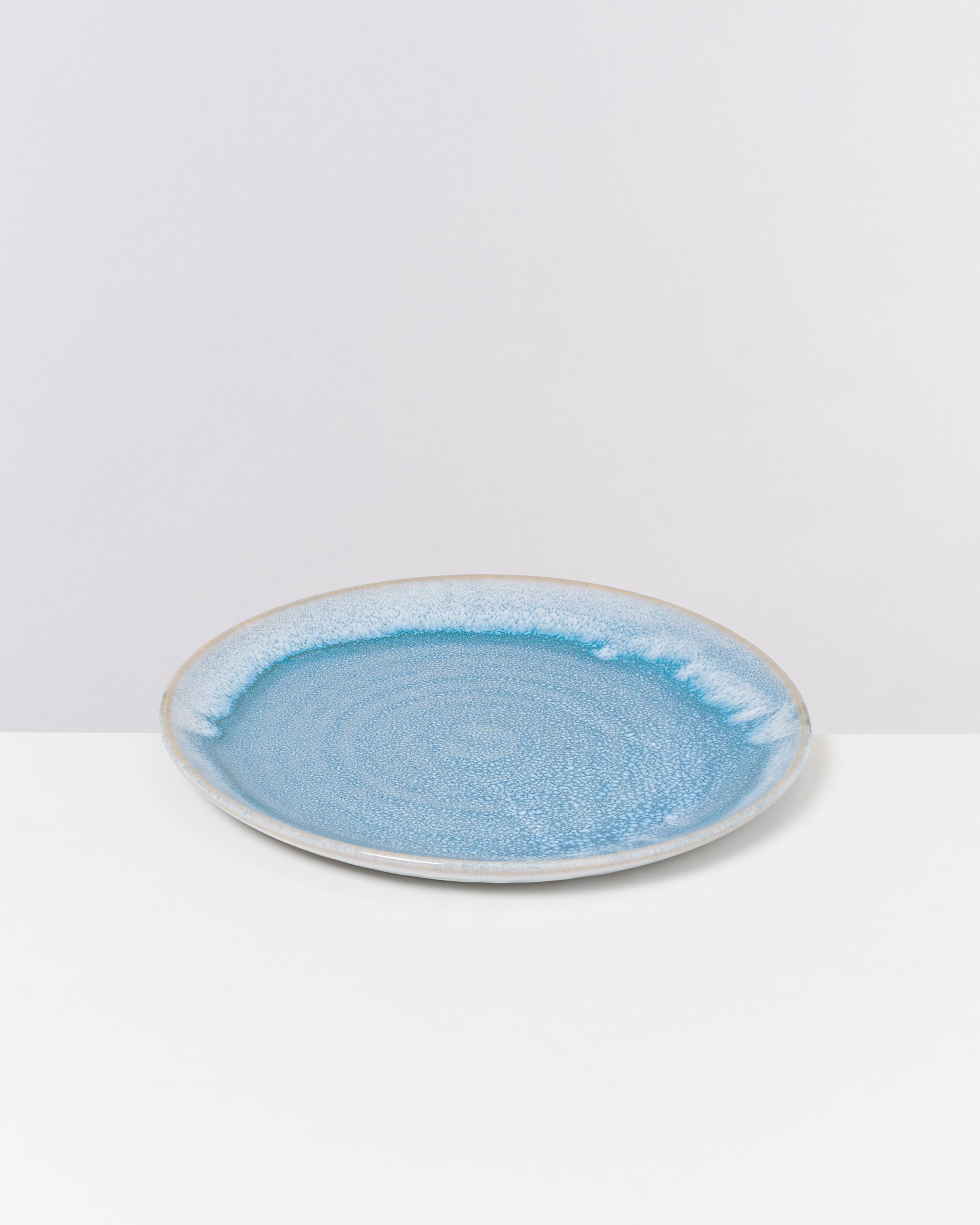 Ein runder Teller mit blauer Glasur und weißem Rand auf einer weißen Oberfläche.