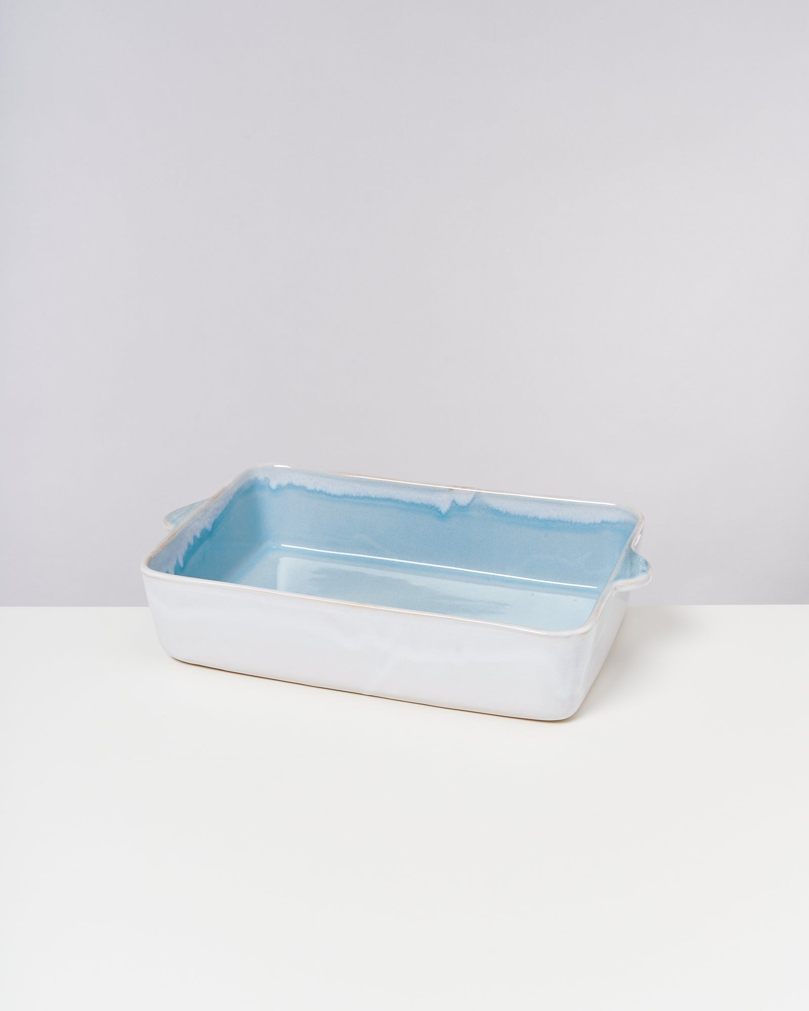 Rechteckige, flache Keramikauflaufform mit blauer Innenseite auf einem weißen Tisch vor grauem Hintergrund.