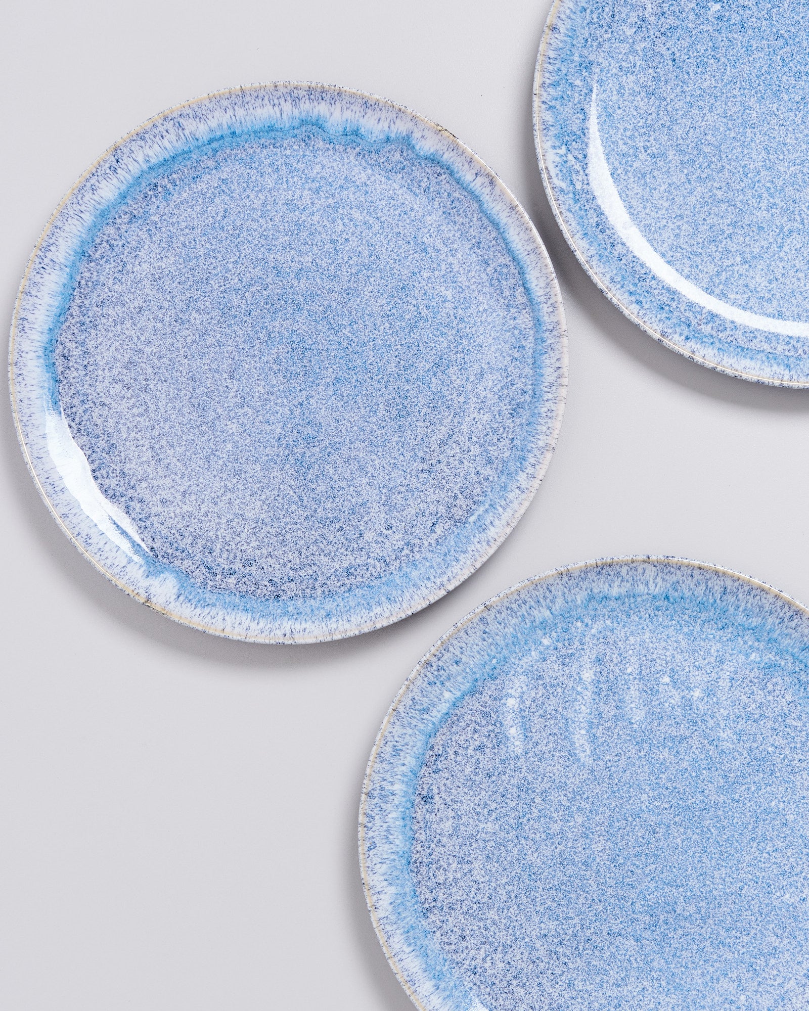 Drei runde, blaue Keramikteller mit gesprenkelter Glasur auf weißem Hintergrund.