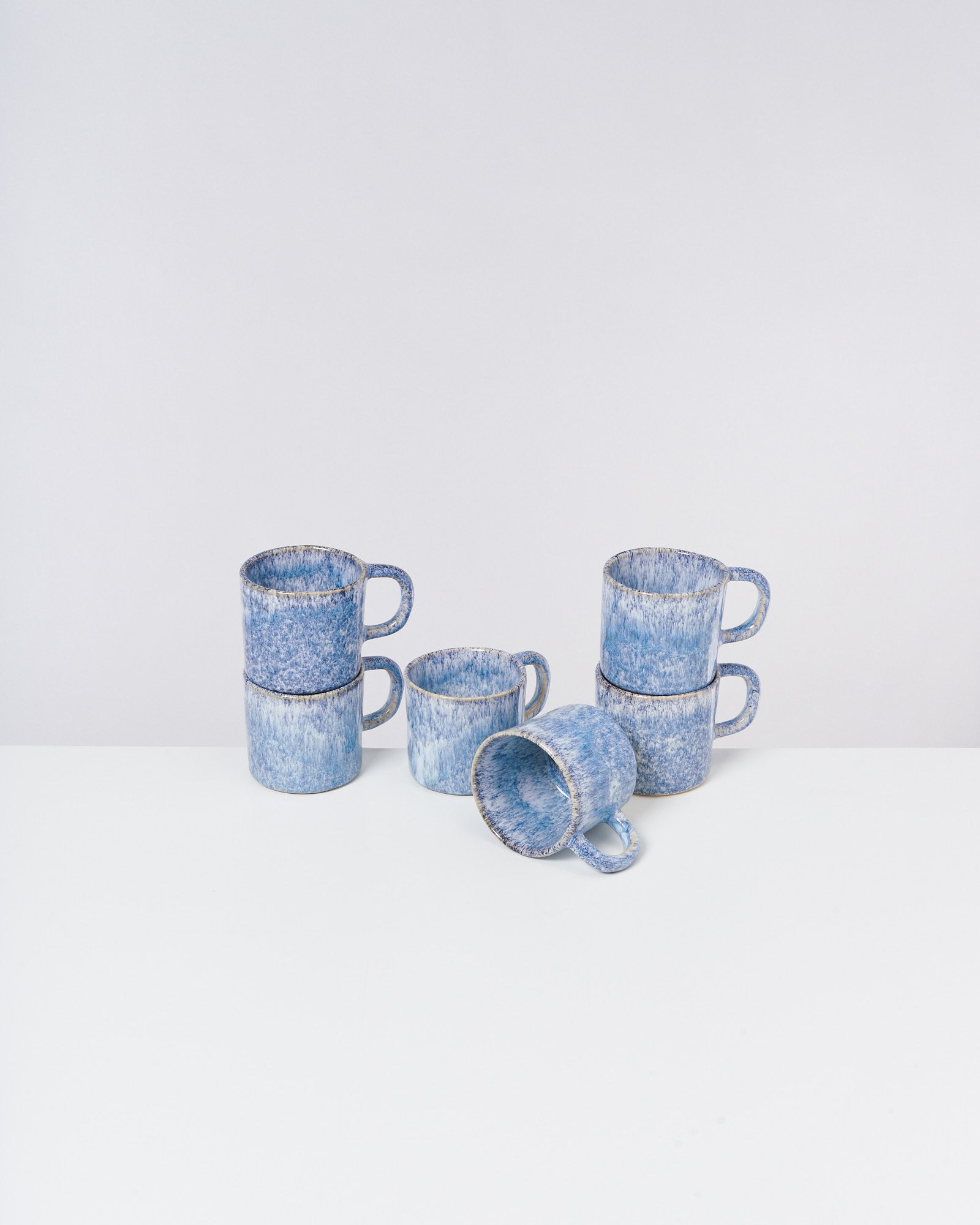 Sechs blaue, gemusterte Tassen sind gestapelt und arrangiert auf einer weißen Oberfläche.
