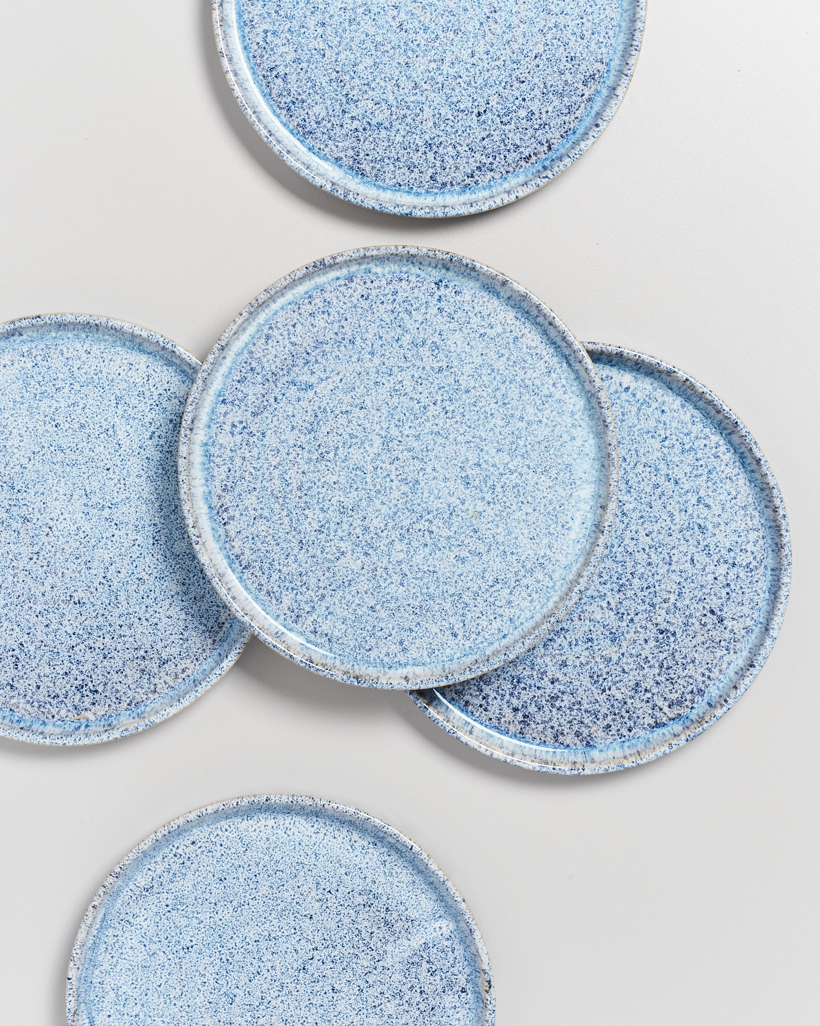 Fünf blaue Keramikteller mit gesprenkeltem Muster liegen überlappend auf einem weißen Hintergrund.