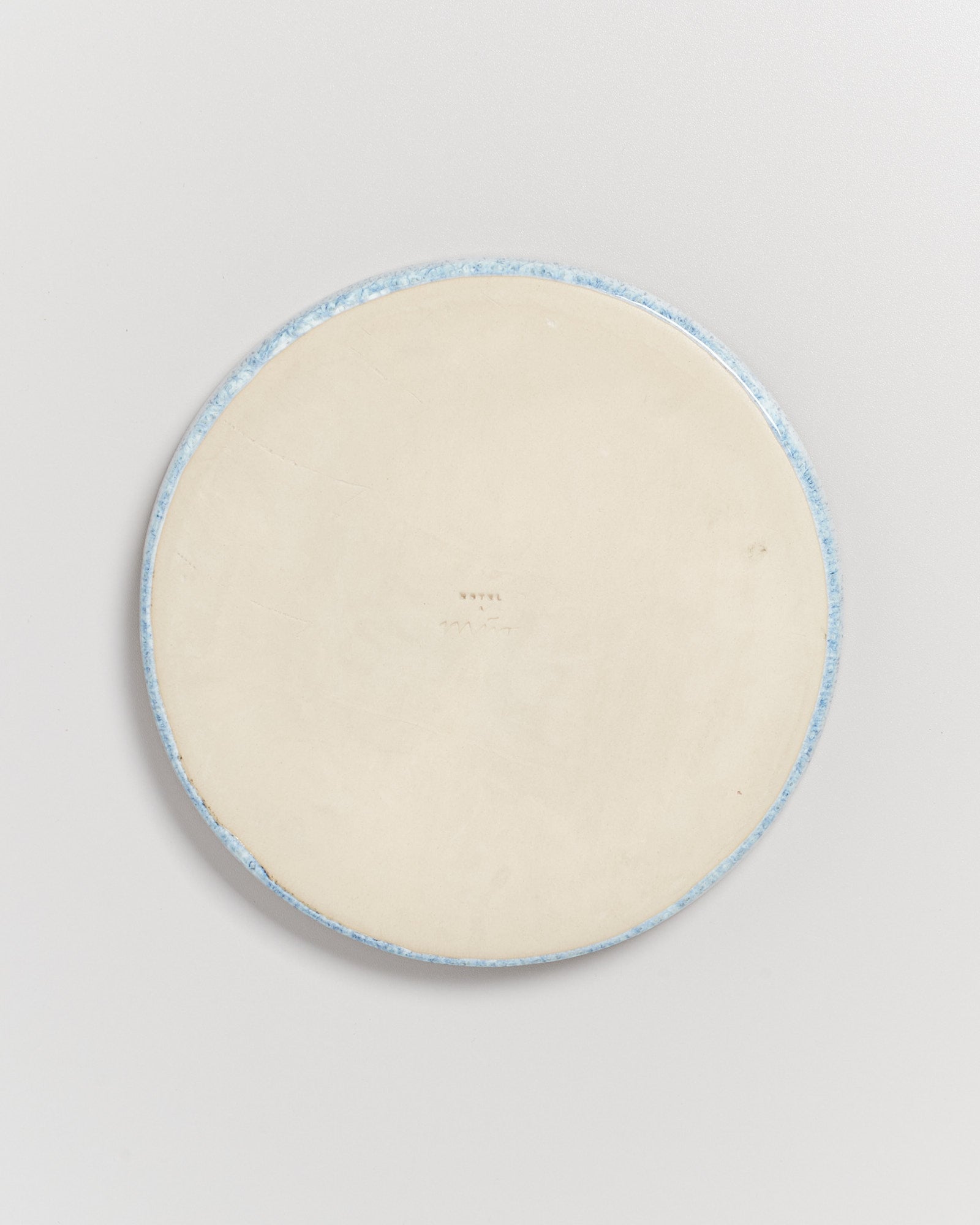 Die Unterseite eines runden Keramiktellers mit blauer Umrandung auf weißem Hintergrund.