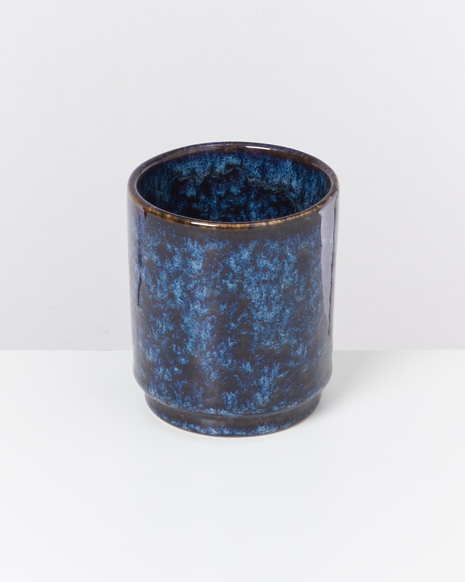 Blauer, zylindrischer Keramikbecher mit marmoriertem Muster auf weißem Hintergrund.