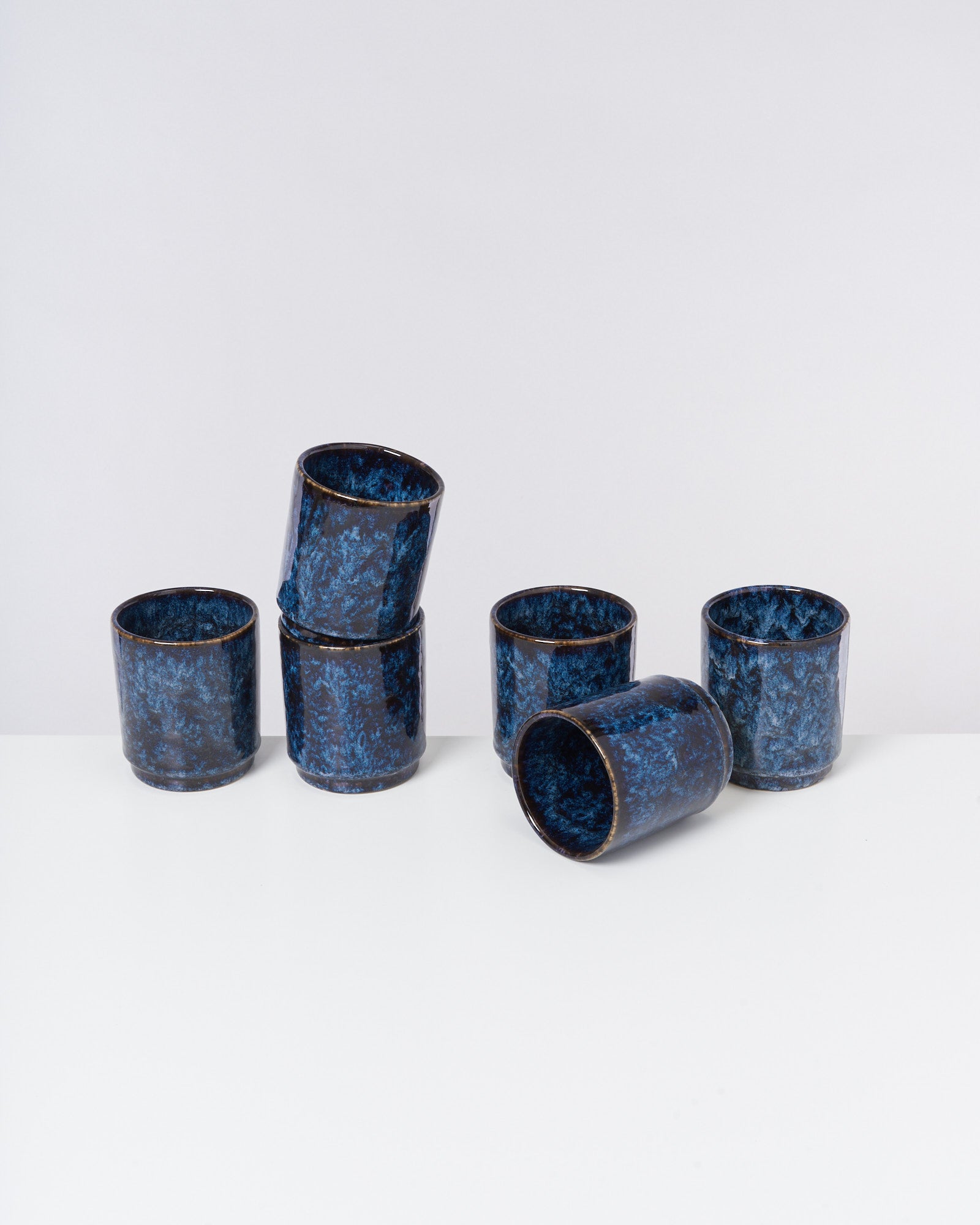 Sechs blaue, marmorierte Becher auf einer weißen Oberfläche, drei stapelnd, drei stehend.