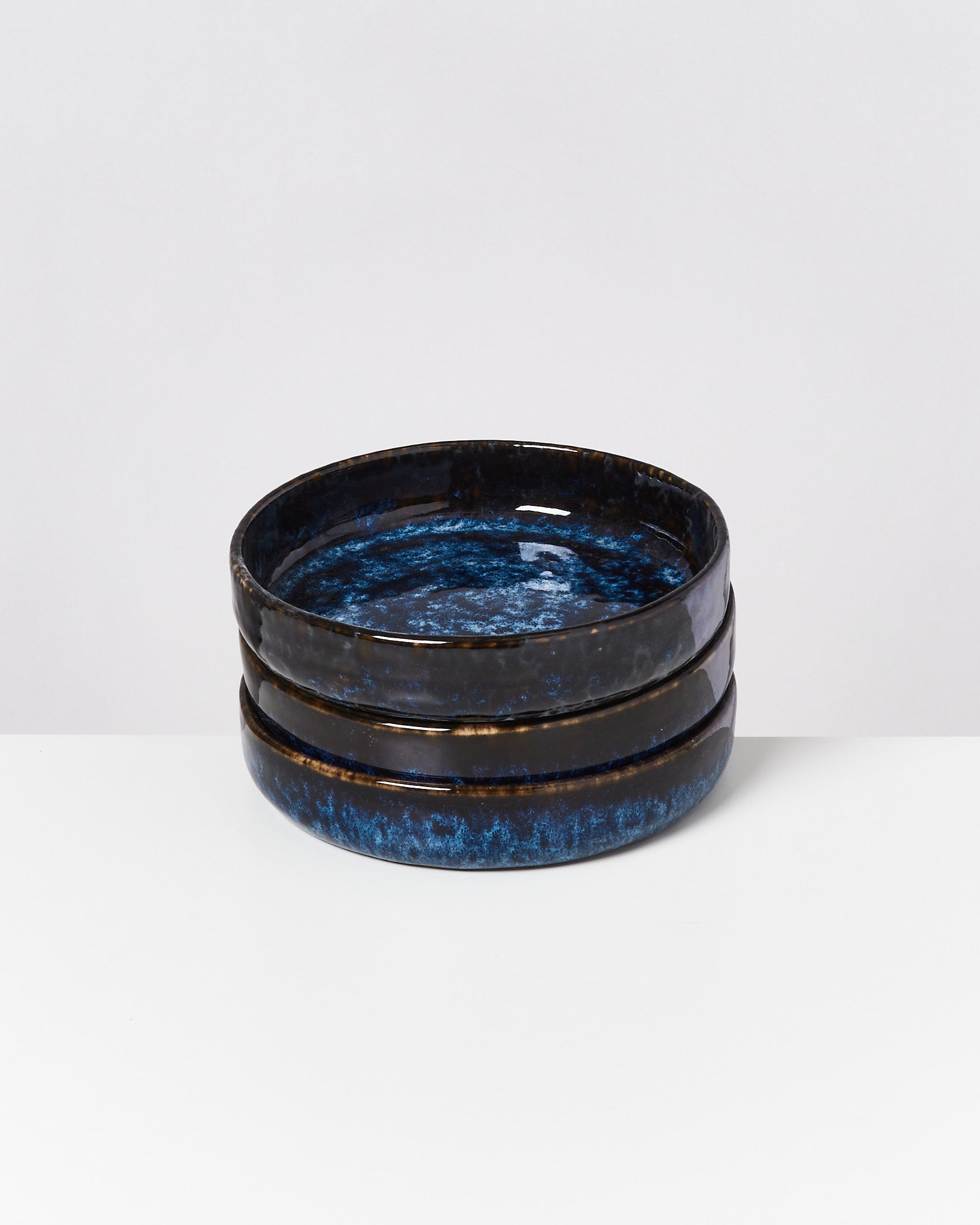 Drei gestapelte blaue, glänzende Keramikschüsseln auf einem weißen Hintergrund.