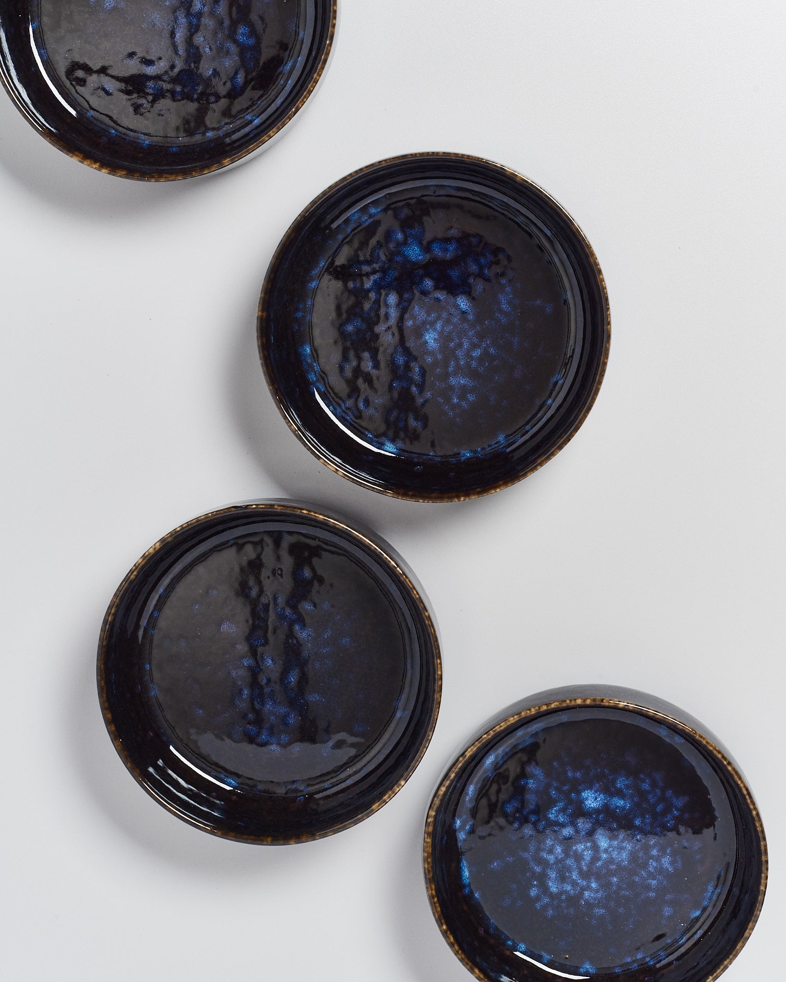 Vier runde, dunkelblaue Keramikteller mit glänzendem Finish auf weißem Hintergrund.