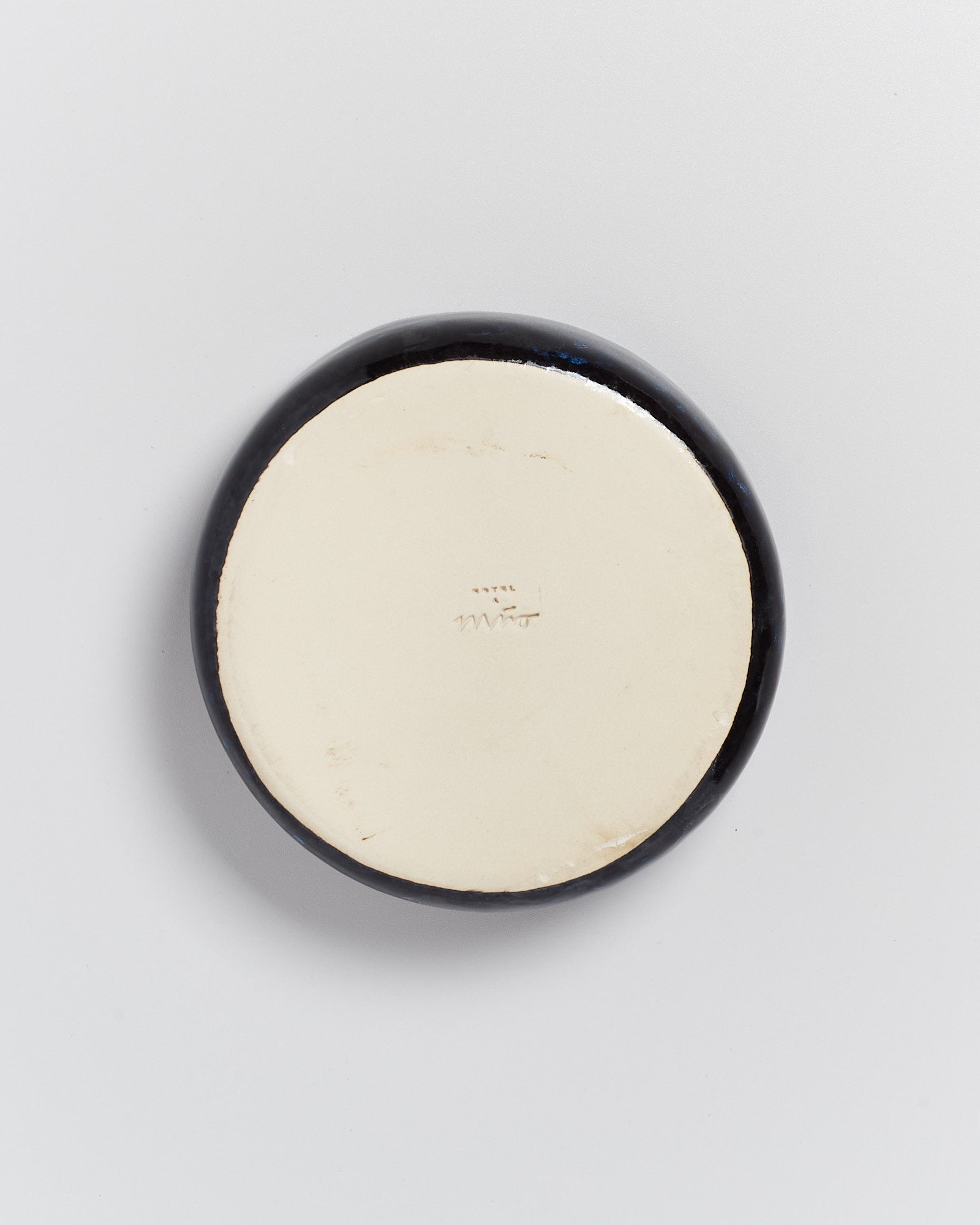 Unterseite einer schwarz-weiß lackierten runden Keramik mit Schriftzug auf hellem Hintergrund.