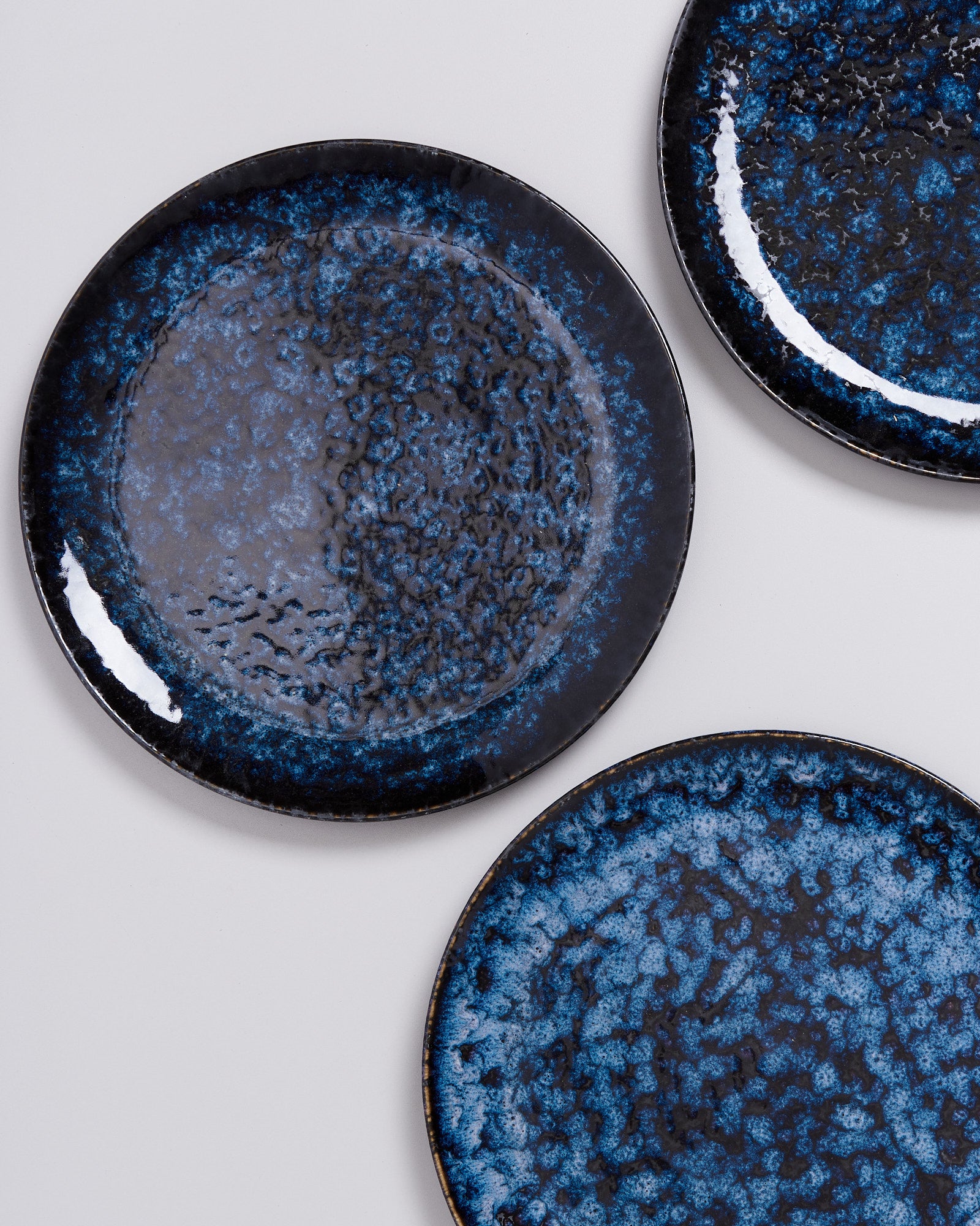 Drei dunkelblaue Teller mit marmorierter Textur auf weißem Hintergrund.
