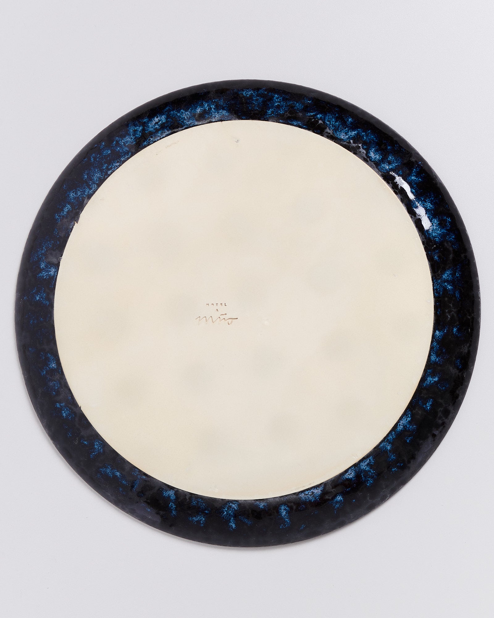 Unterseite eines runden Tellers mit dunkel-blauem Rand und einer Signatur in der Mitte.