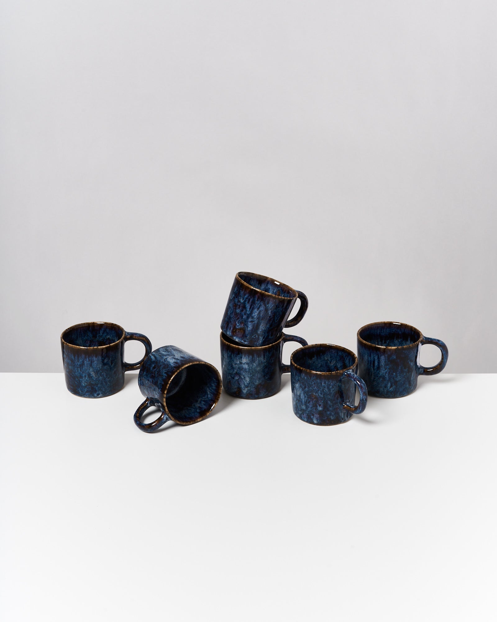 Sechs blaue Tassen auf einem weißen Tisch, von denen vier gestapelt und zwei daneben platziert sind.