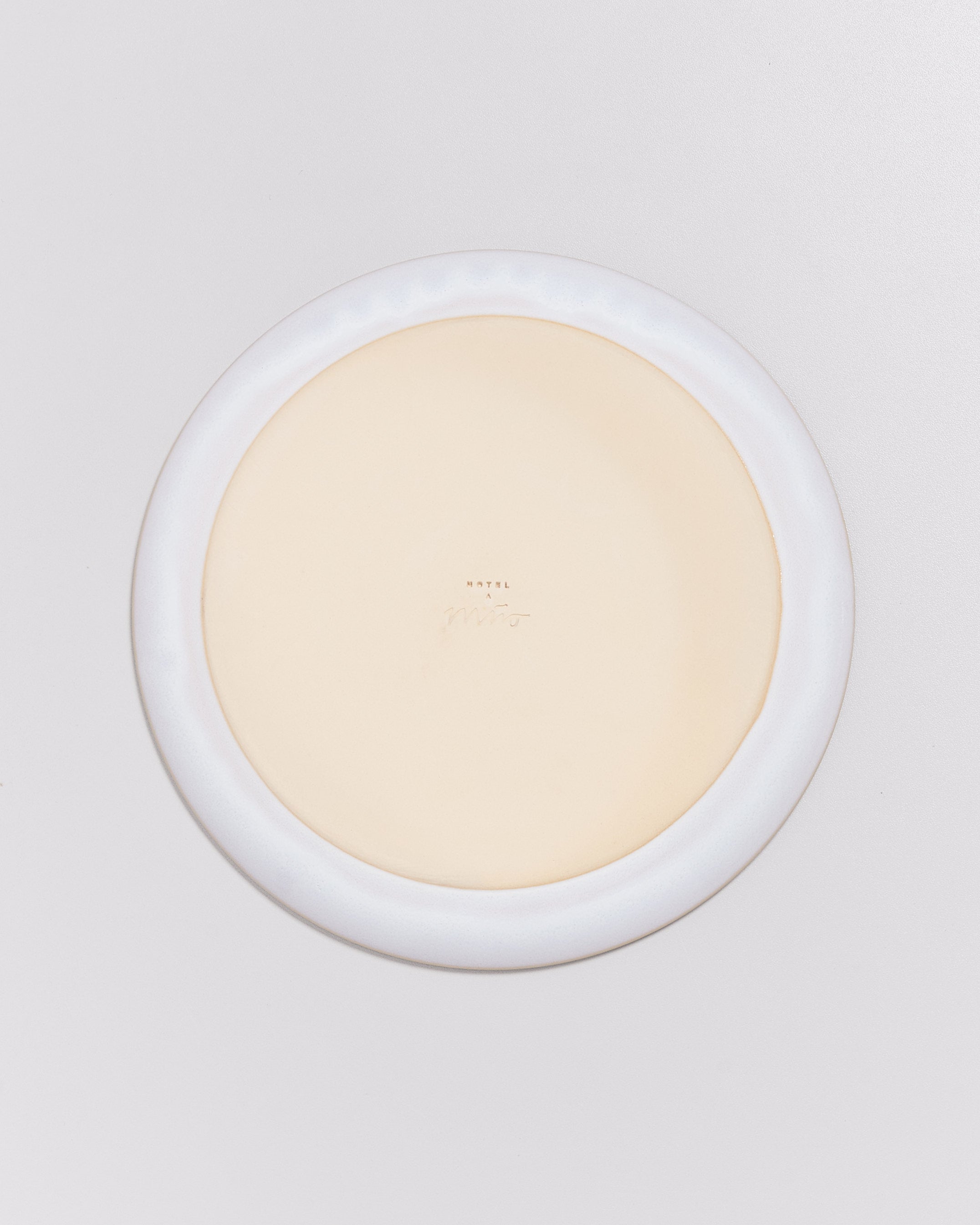 Rückseite eines hellen Tellers mit weißem Rand und eingravierter Aufschrift in der Mitte, auf weißem Hintergrund.