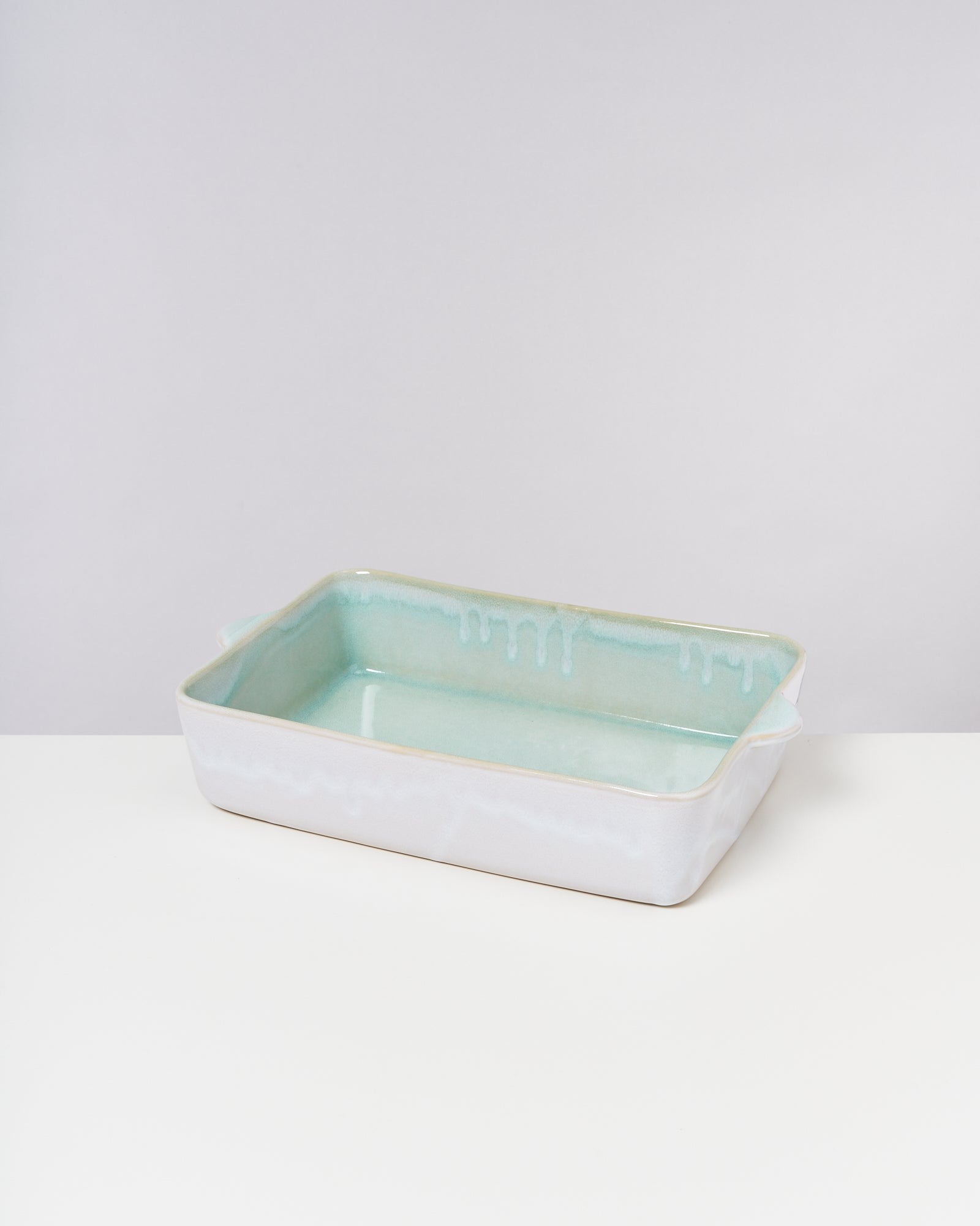 Rechteckige, pastellfarbene Keramikbackform mit weißen Streifen, auf einem weißen Tisch mit grauem Hintergrund.