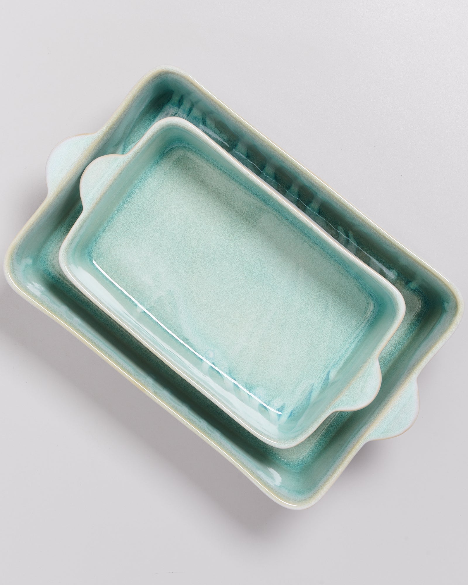 Zwei türkisfarbene, ineinander gestapelte rechteckige Keramikauflaufformen auf grauem Hintergrund.