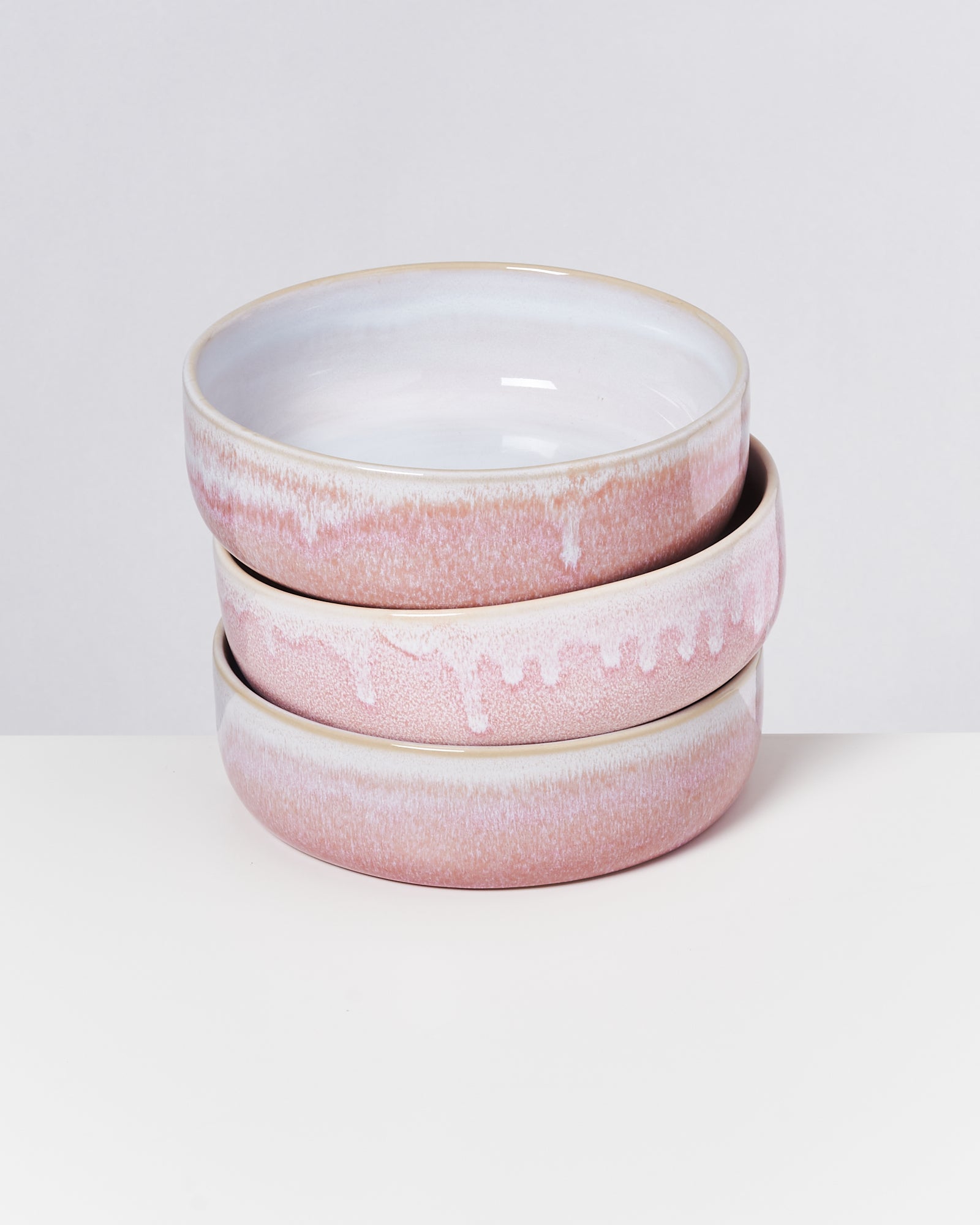 Drei übereinander gestapelte rosa und weiße Keramikschalen auf weißem Hintergrund.