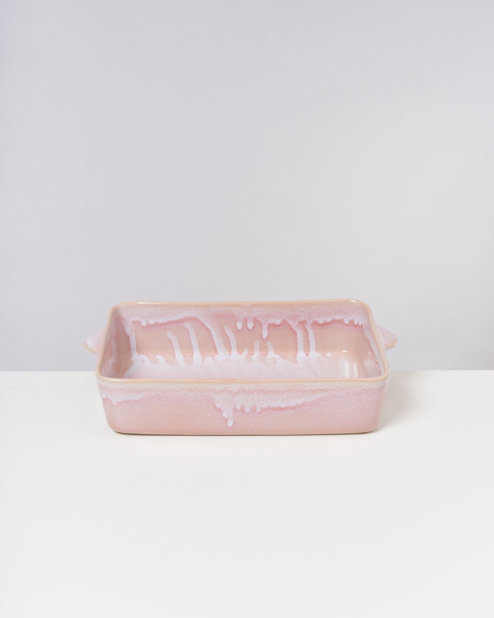 Rechteckige, rosafarbene Keramikauflaufform mit weißen, tropfenartigen Mustern auf einem weißen Hintergrund.
