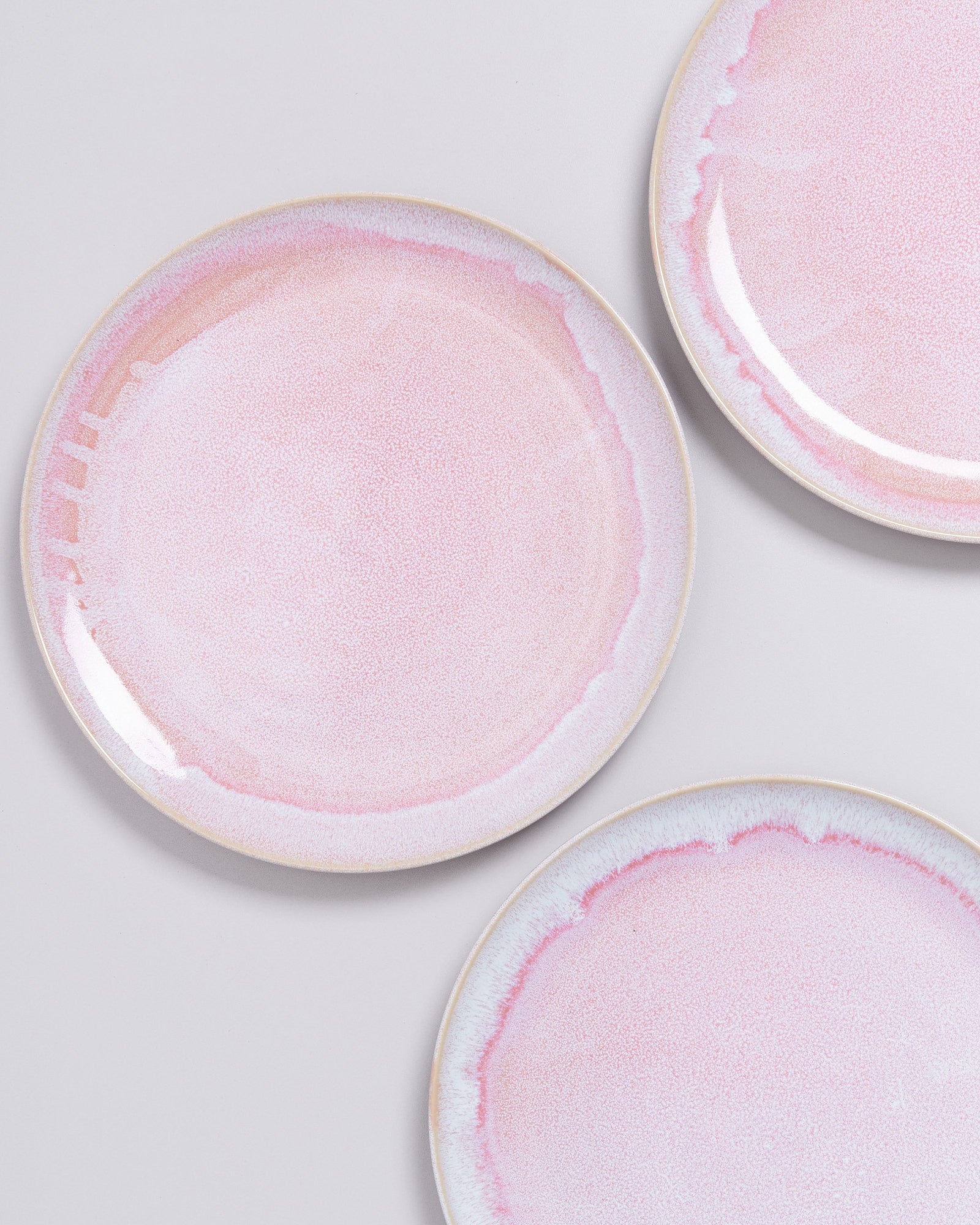 Drei rosa Keramikteller mit feiner Musterung auf einem weißen Hintergrund.