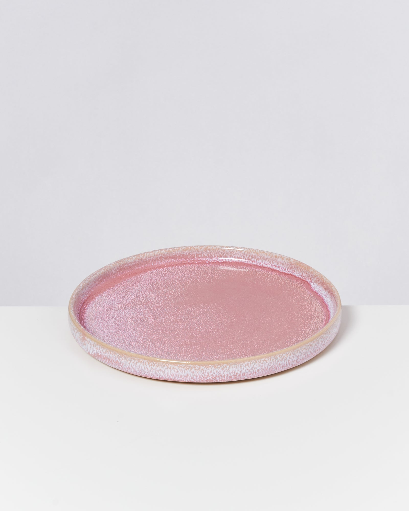 Rosafarbener Keramikteller mit glatter Oberfläche auf einem weißen Hintergrund.