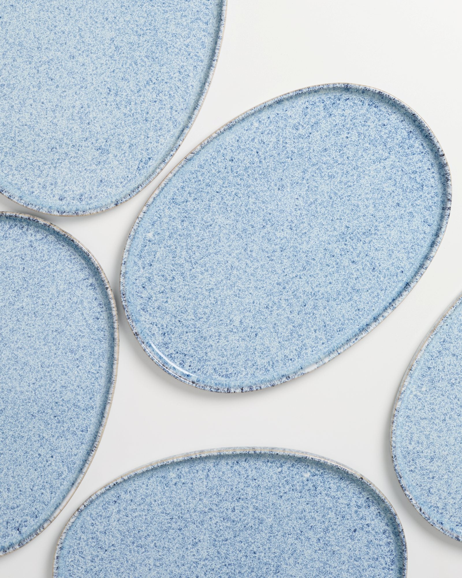 Fünf ovale, hellblaue Keramikteller mit gesprenkeltem Muster liegen auf einem weißen Hintergrund.