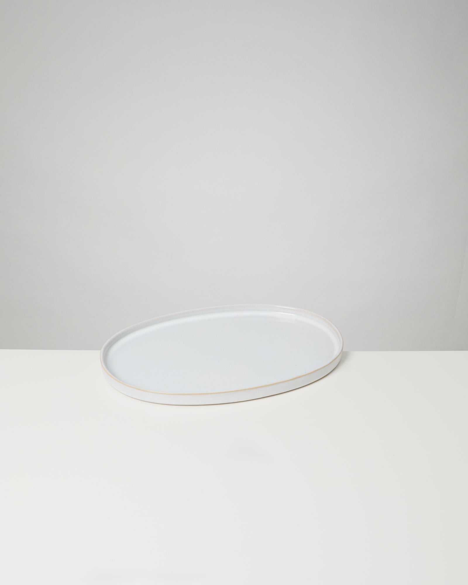 Ovaler, weißer Teller auf einem hellen Untergrund vor grauem Hintergrund.