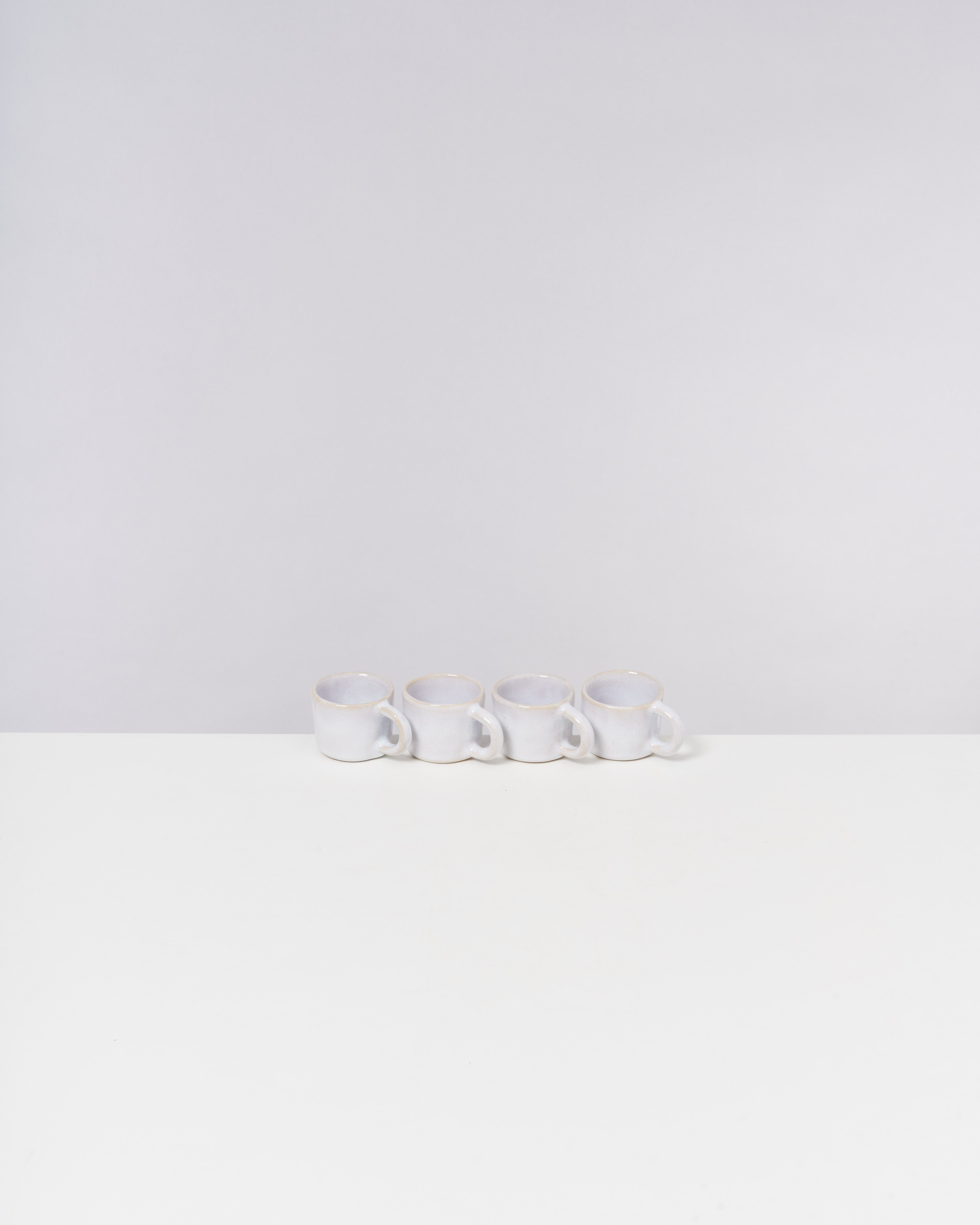 Vier weiße Tassen stehen in einer Reihe auf einem weißen Tisch mit grauem Hintergrund.