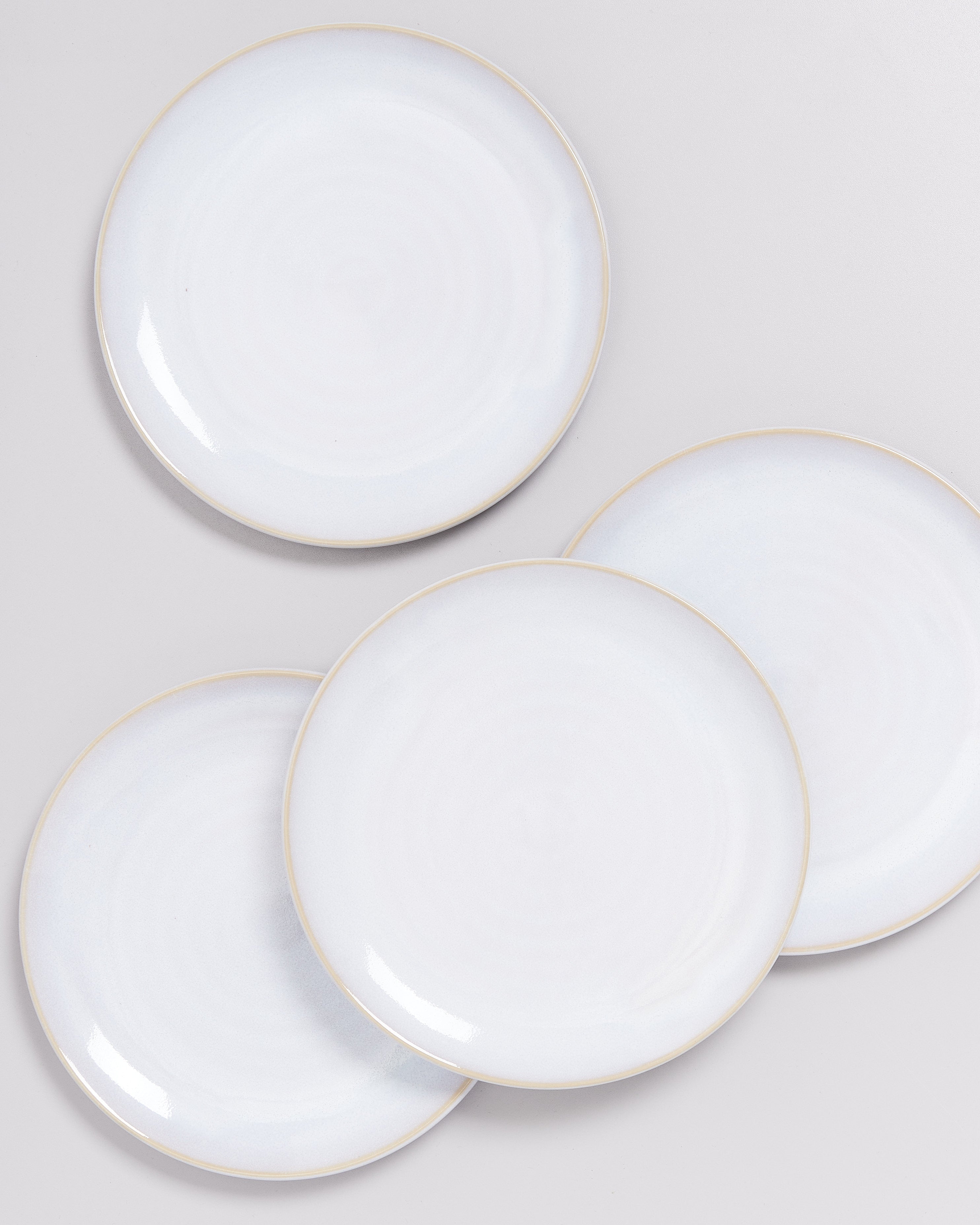 Vier weiße Teller mit leichtem Farbverlauf und dünnem Rand liegen übereinander auf einer grauen Fläche.