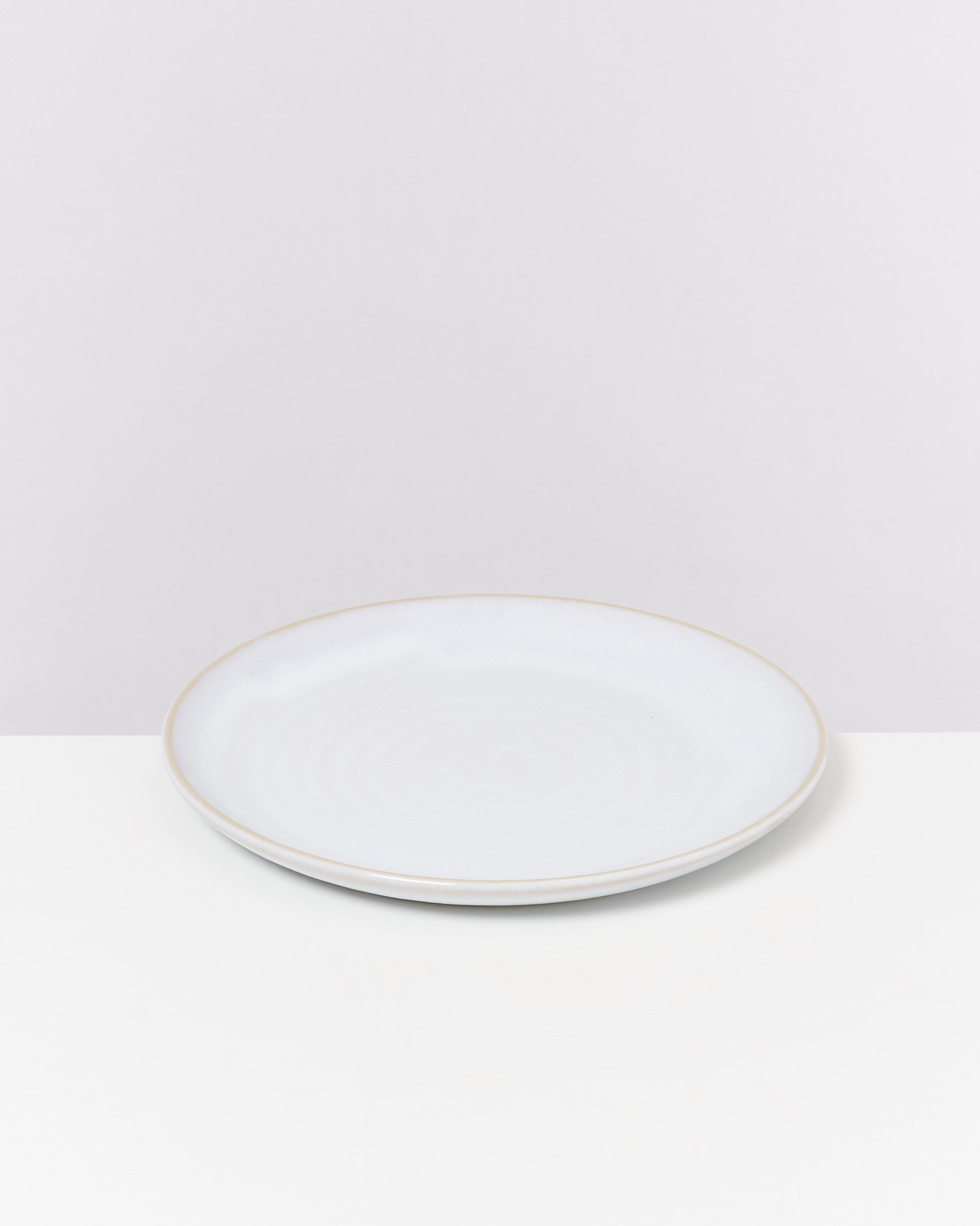 Weißer, flacher Teller auf weißem Hintergrund.