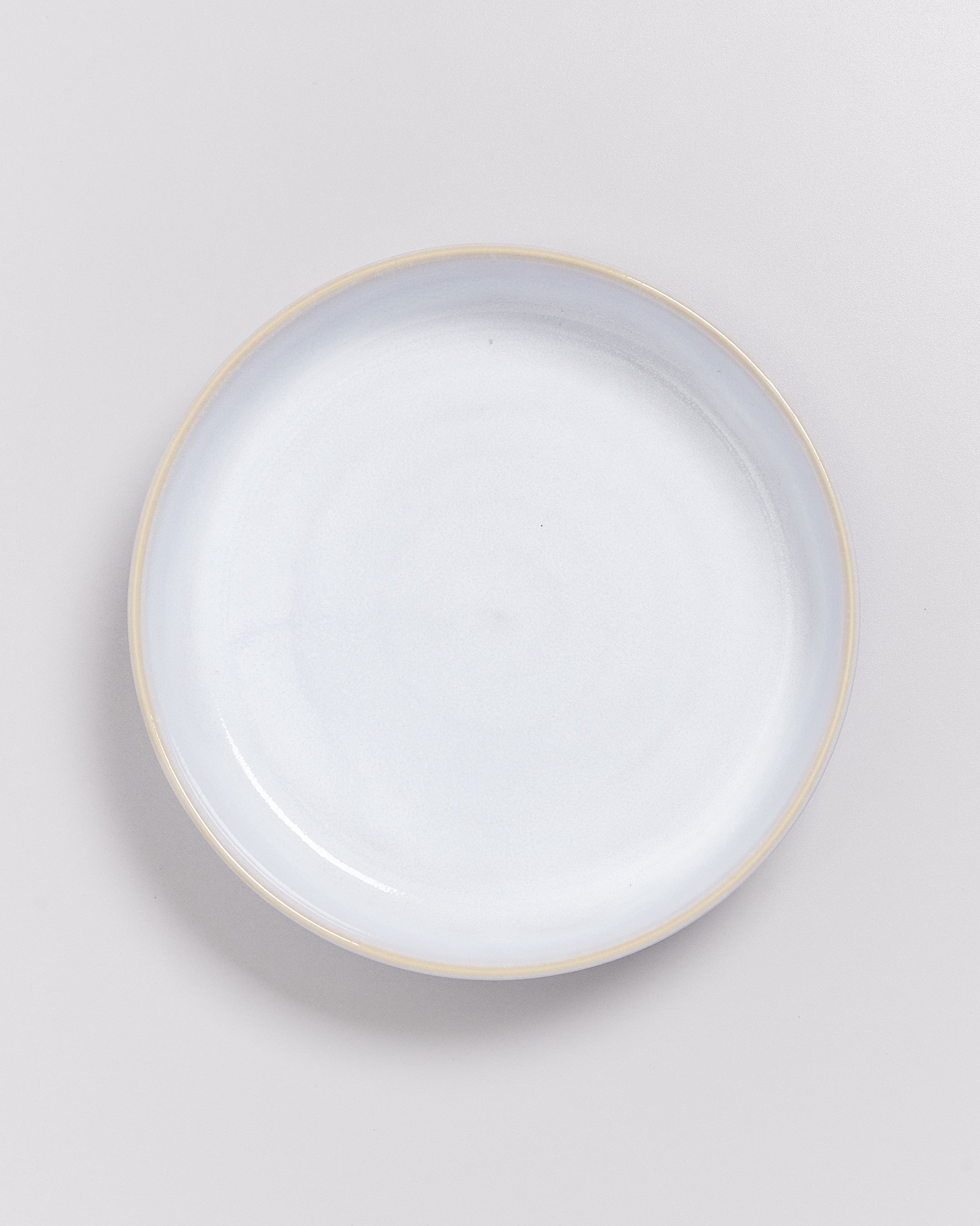 Ein runder, heller Teller mit einem dünnen, goldfarbenen Rand auf weißem Hintergrund.