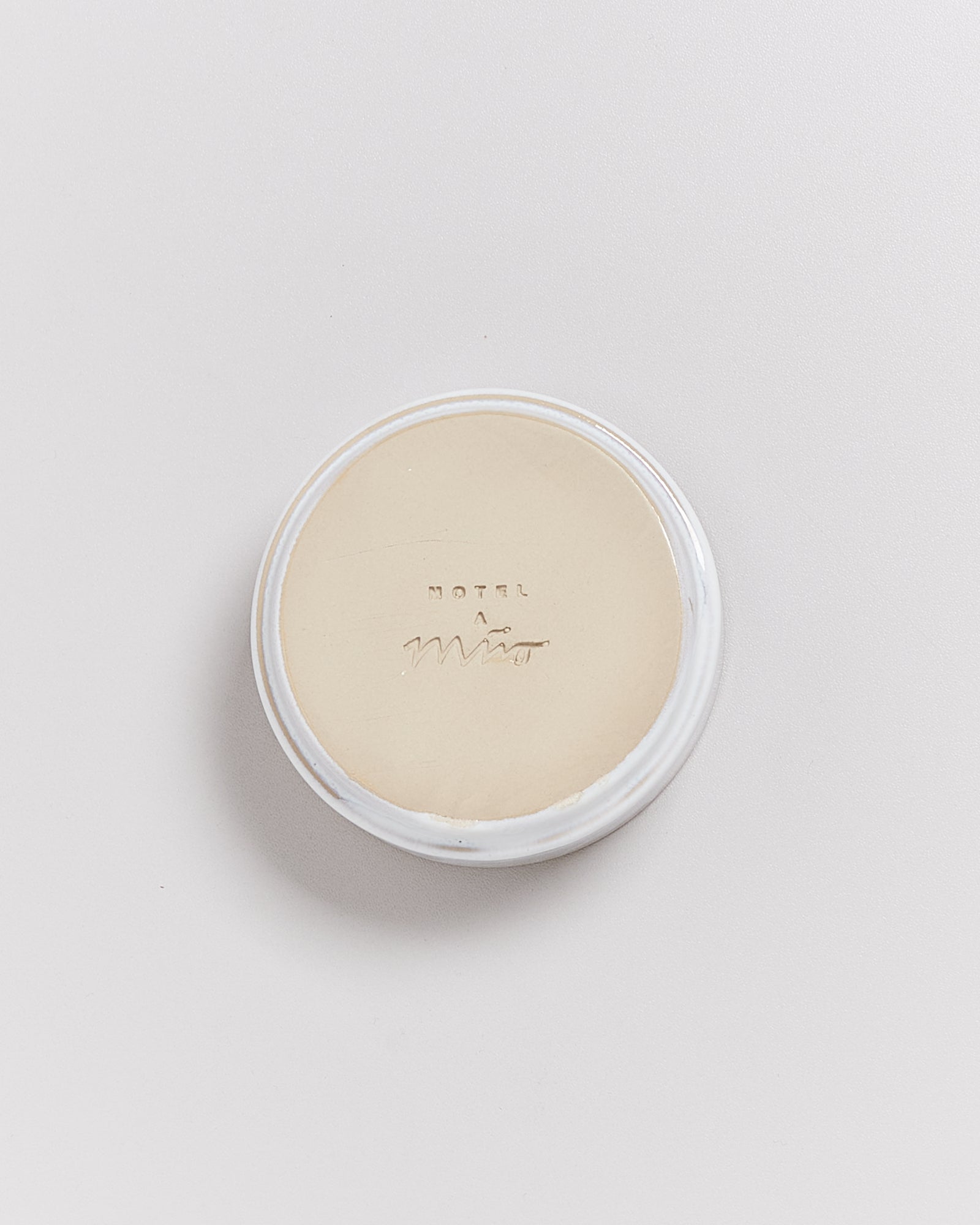 Eine runde Seife mit der Prägung "HOTEL" und "Mio" auf einer weißen Oberfläche liegt zentral sichtbar.