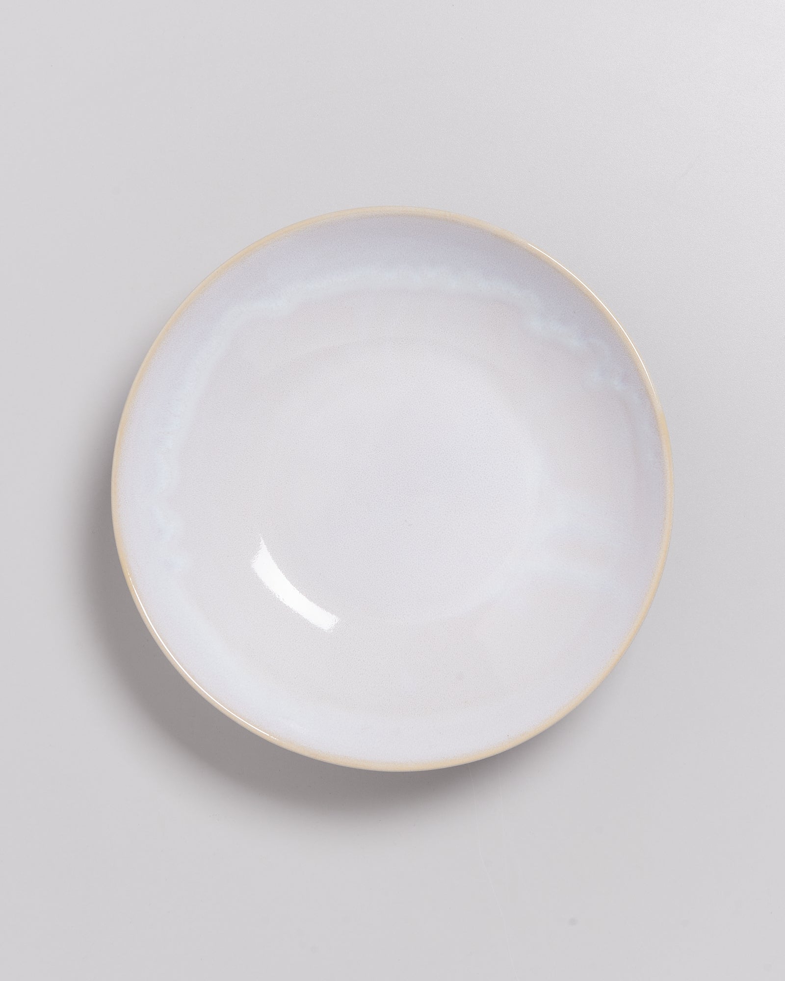 Eine schlichte, runde, weiße Keramikschale mit leicht glänzender Oberfläche auf grauem Hintergrund.