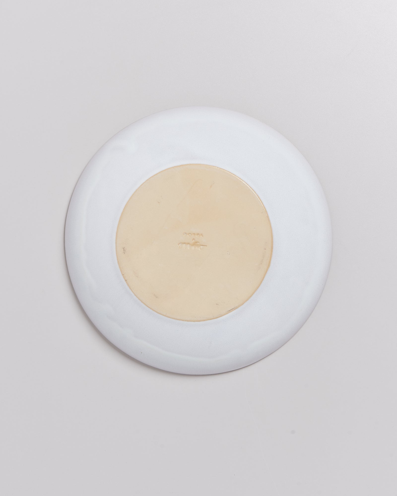 Die Rückseite eines weißen Tellers mit beigem Zentrum und eingeprägter Marke in der Mitte.