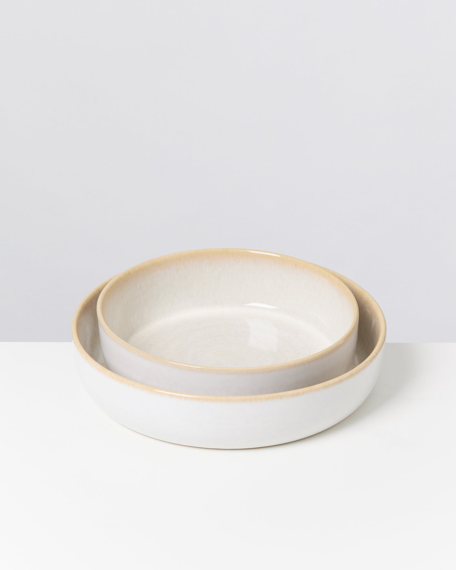 Zwei ineinander gestapelte, weiße Keramikschalen mit leicht bräunlichem Rand auf einer weißen Oberfläche.