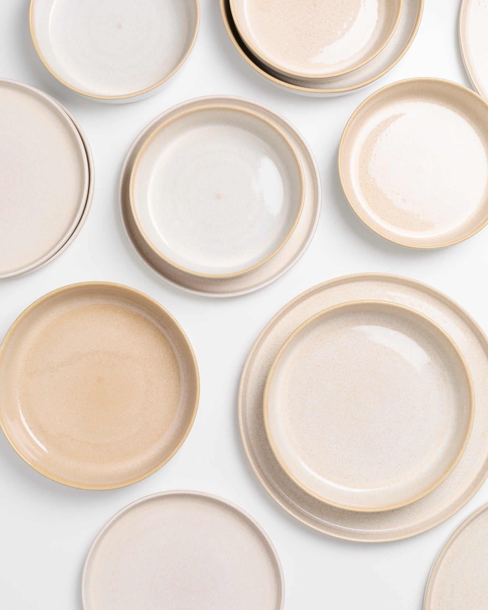 Mehrere beigefarbene Keramikteller in verschiedenen Größen verteilt auf weißem Hintergrund.