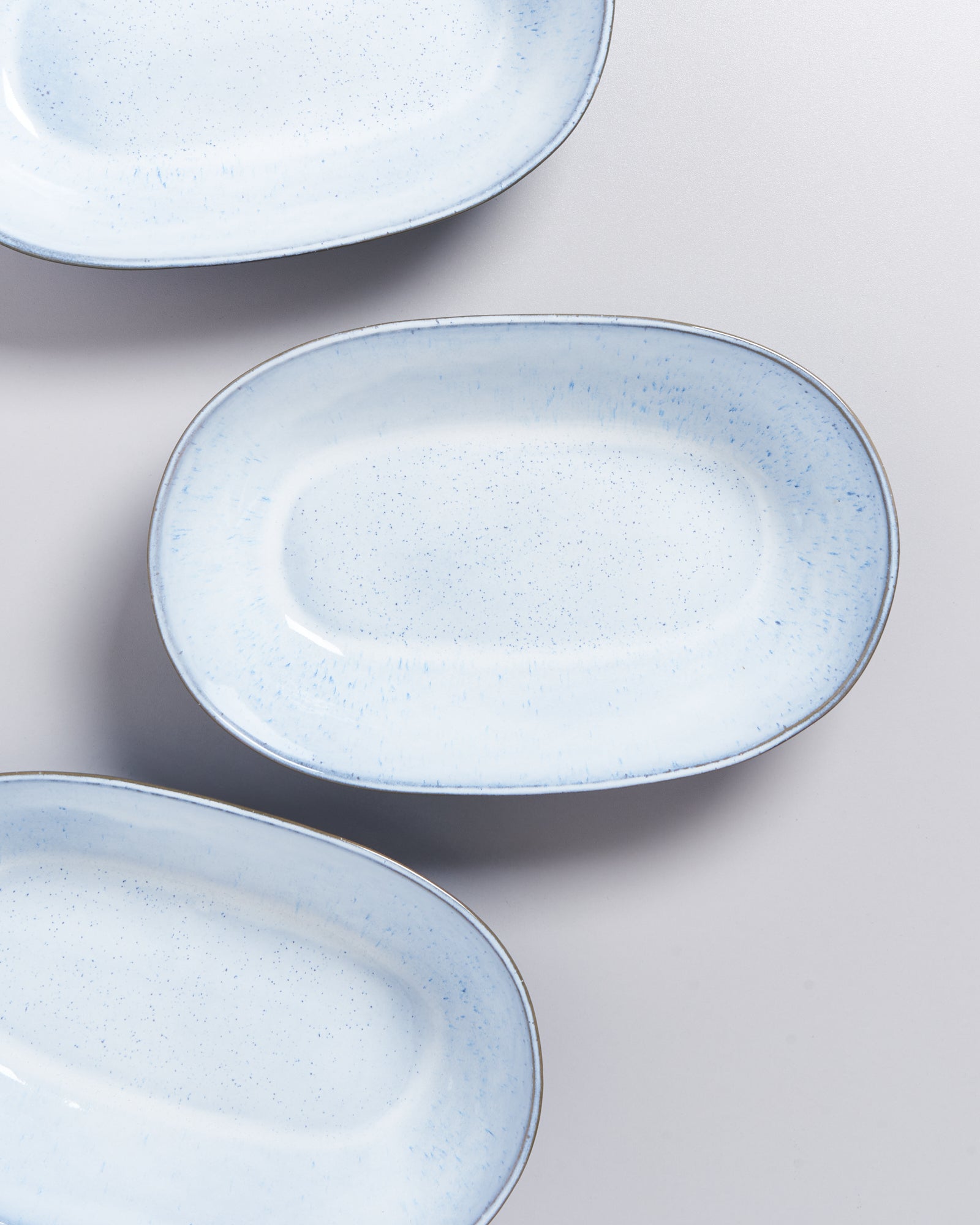 Drei ovale, hellblaue Teller mit gesprenkeltem Muster auf einer grauen Oberfläche.