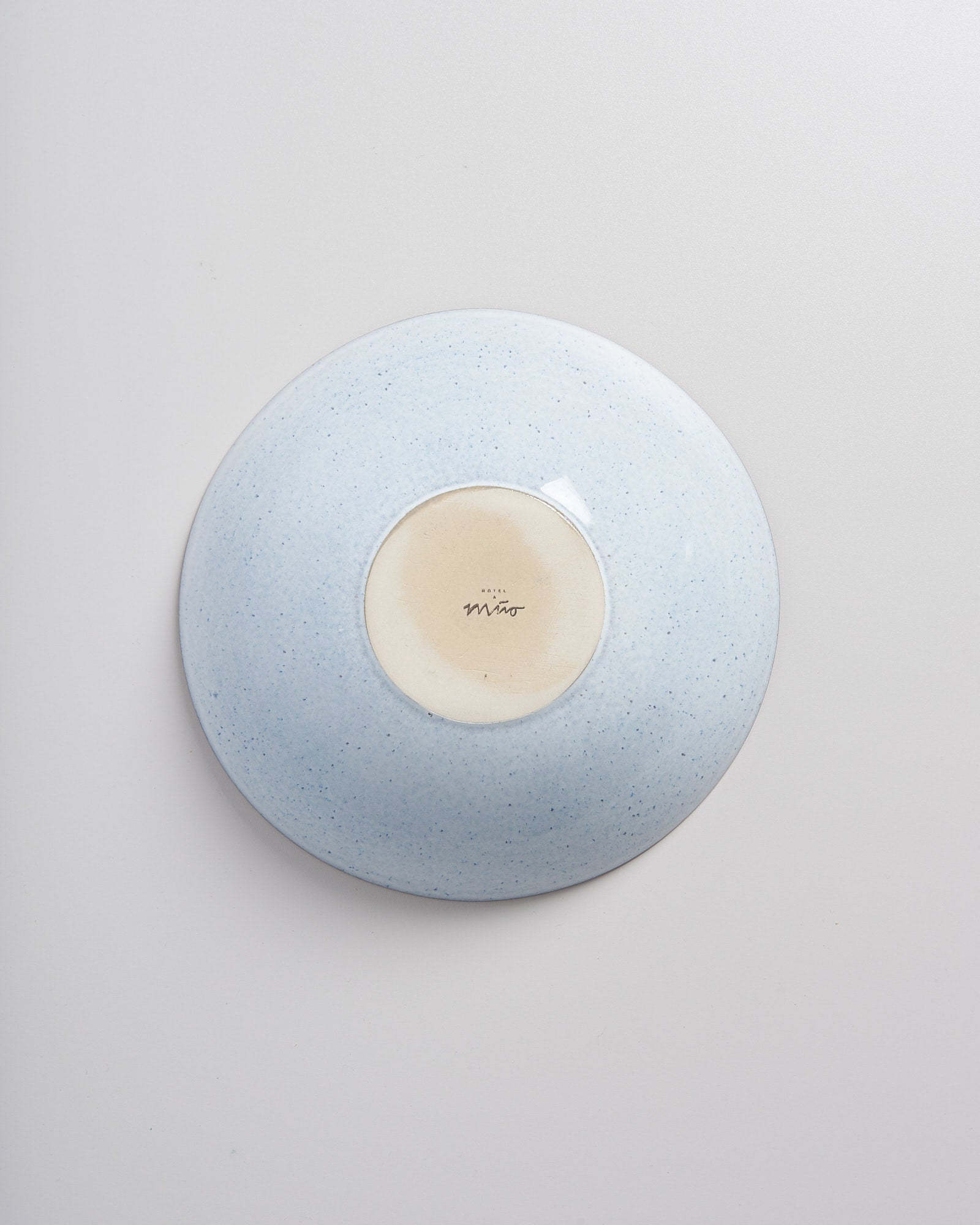 Die Unterseite eines weißen Keramiktellers mit blauer Sprenkelung und einer Marke in der Mitte.